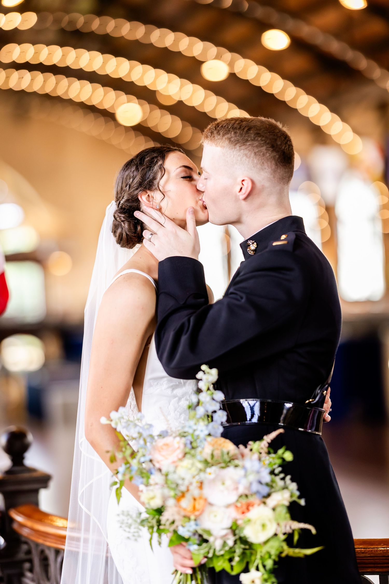 A wedding couple shares romantic kisses under warm glowing lights with delicate floral bouquet details.