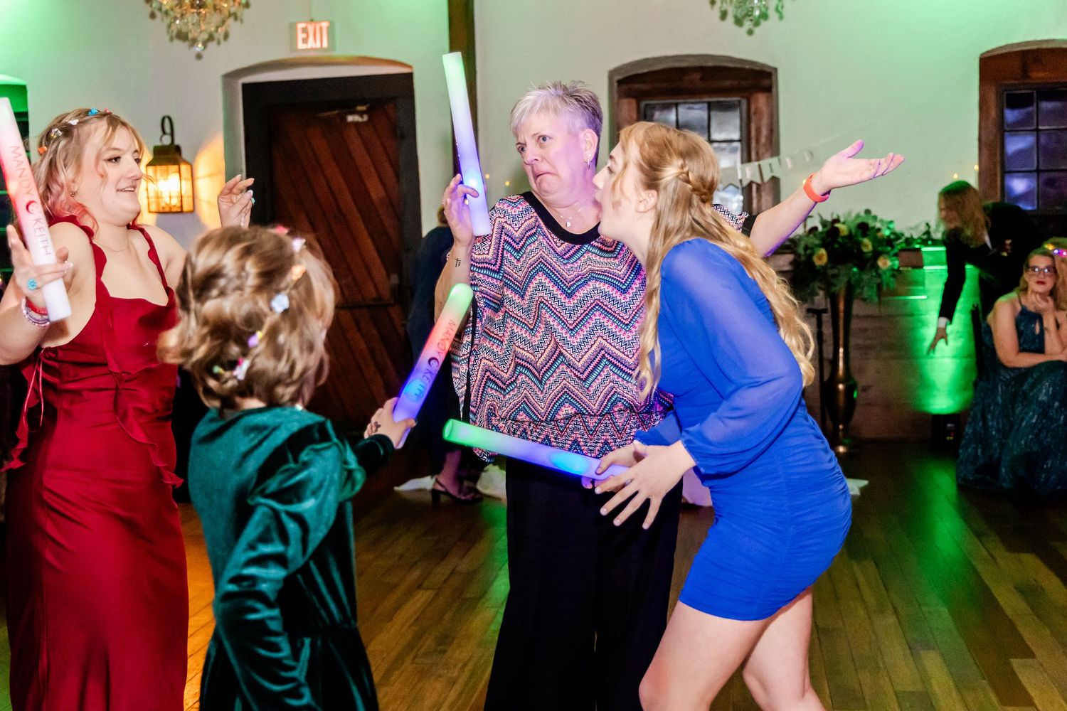 Wedding guests dancing energetically under colorful lighting at an indoor reception.