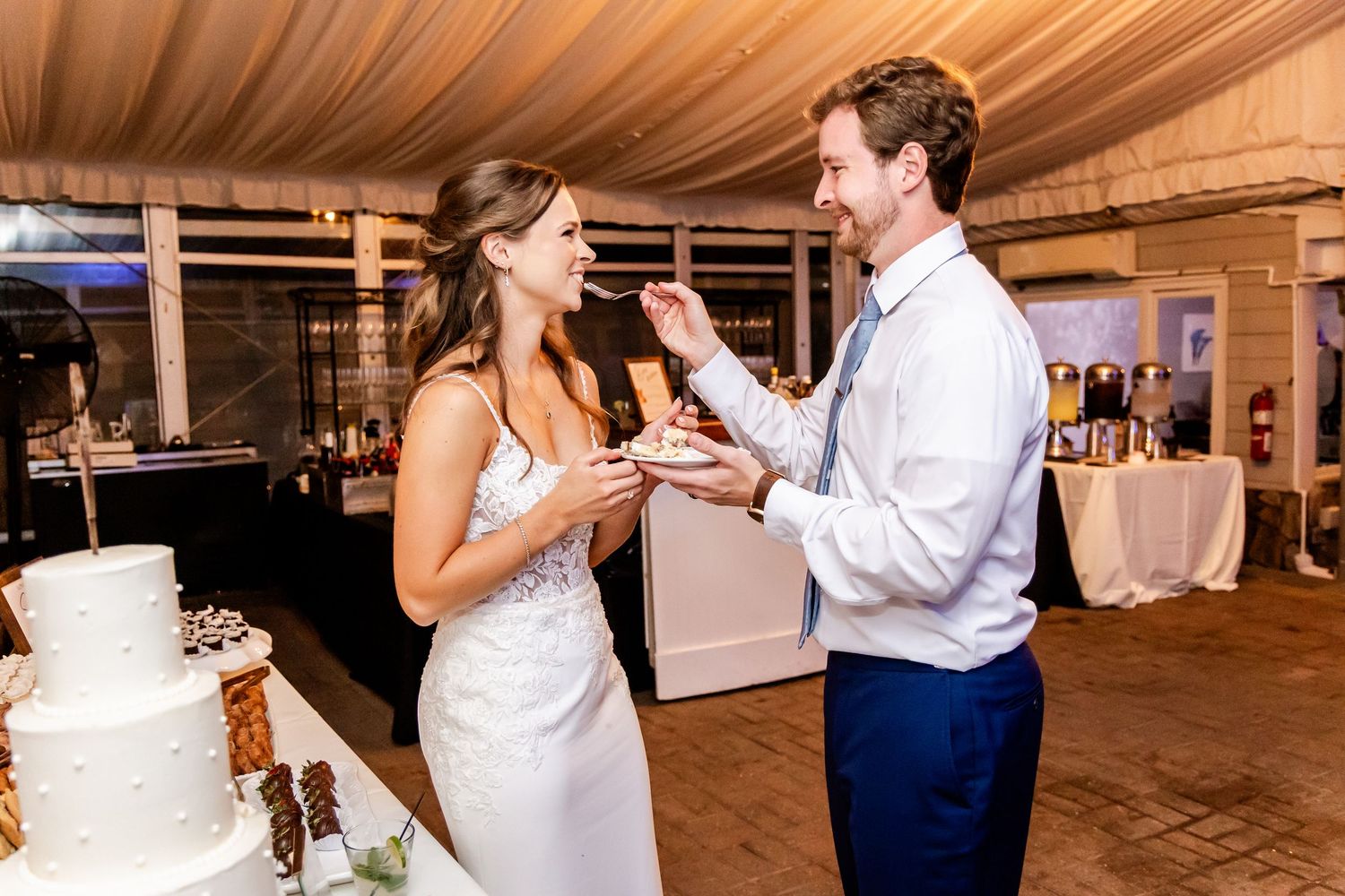 A couple feeds each other wedding cake during their reception celebration.