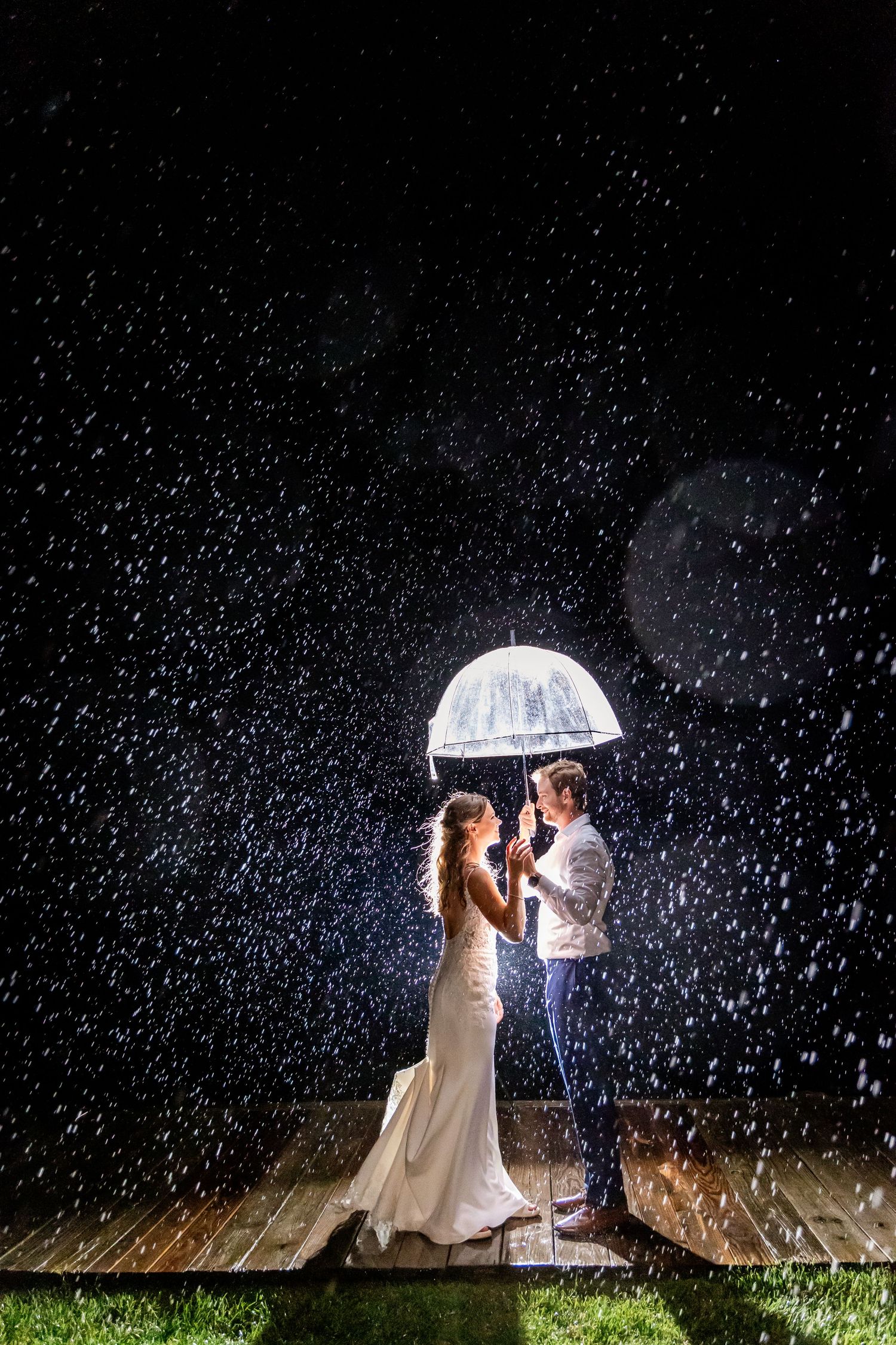 A couple shares a romantic moment under an umbrella in the rain at night.