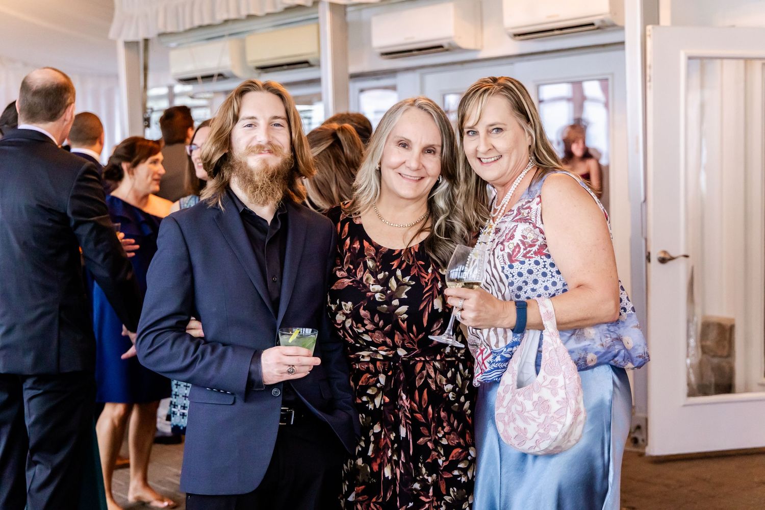 Wedding guests smile and celebrate at an indoor reception venue with bright lighting.