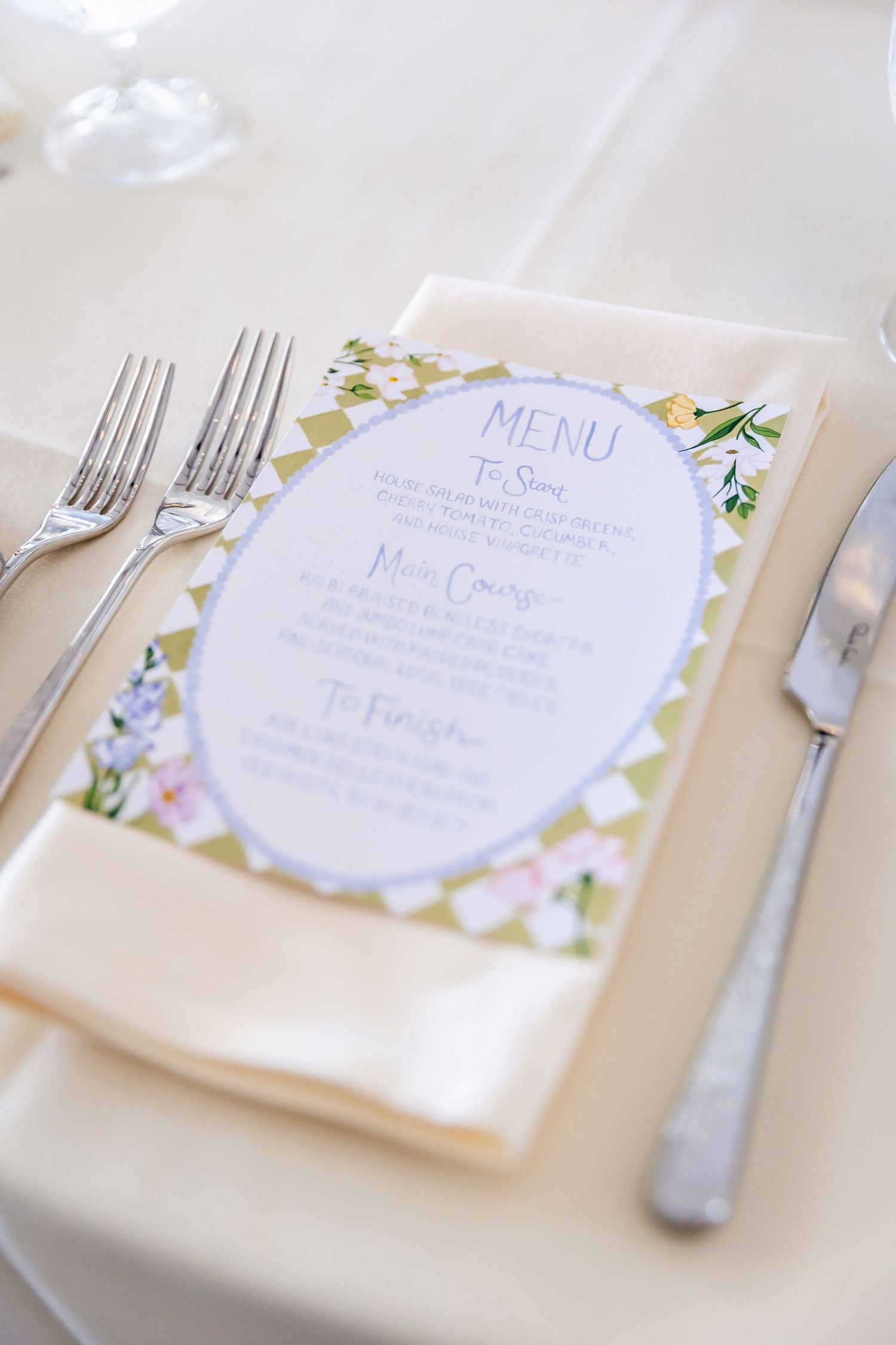 Elegant wedding menu cards with floral designs and silverware placed on cream colored tables.