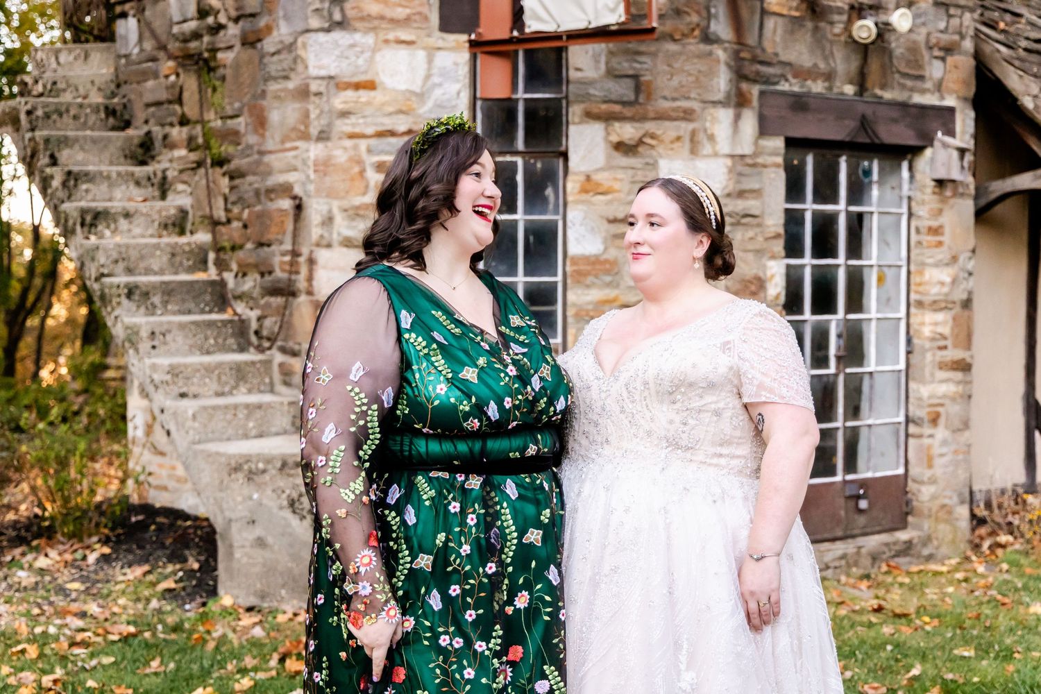 Intimate outdoor wedding moment beside stone cottage with autumn leaves falling in background.