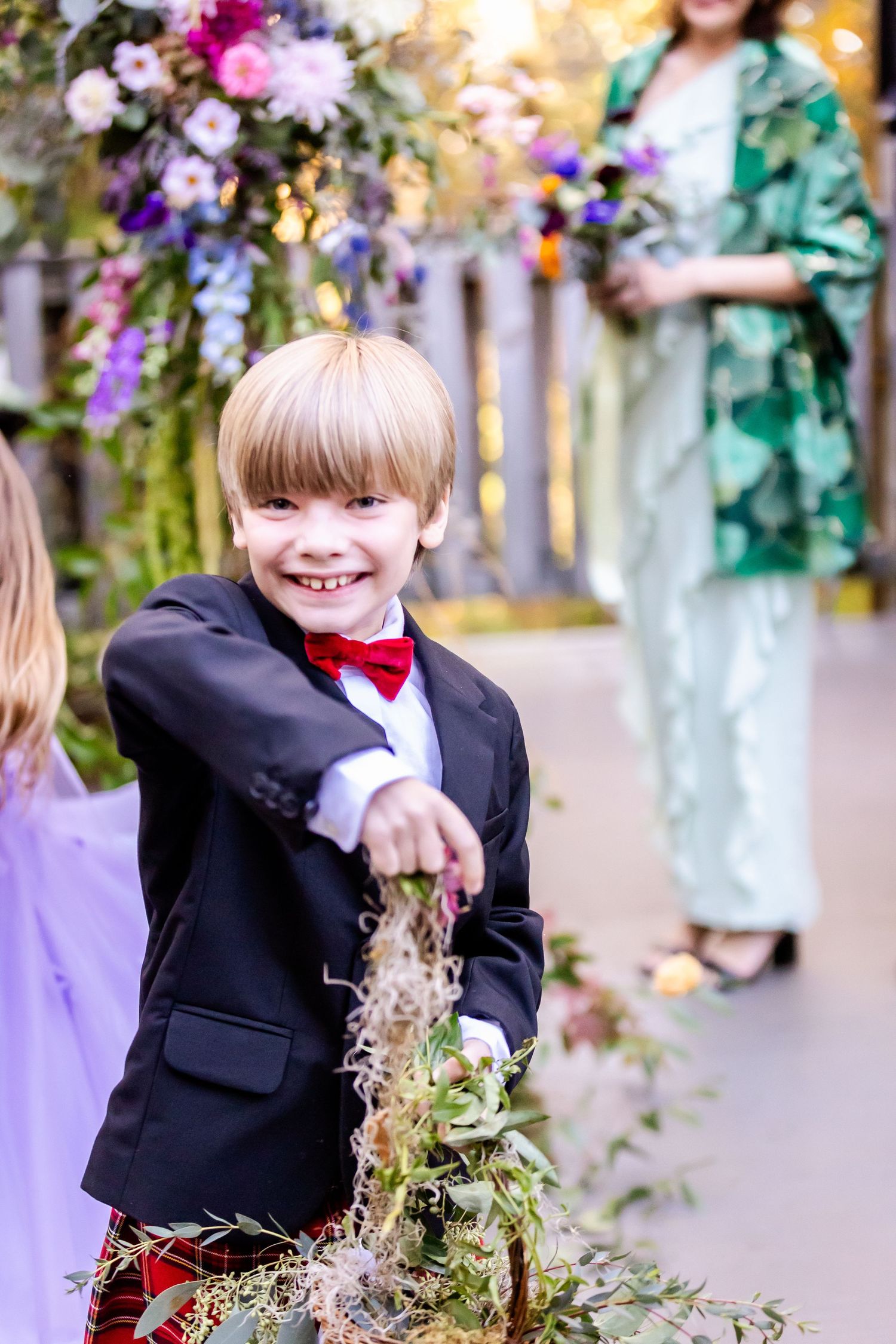 Young ring bearer in a black suit and bow tie playing with decorations at a wedding celebration.