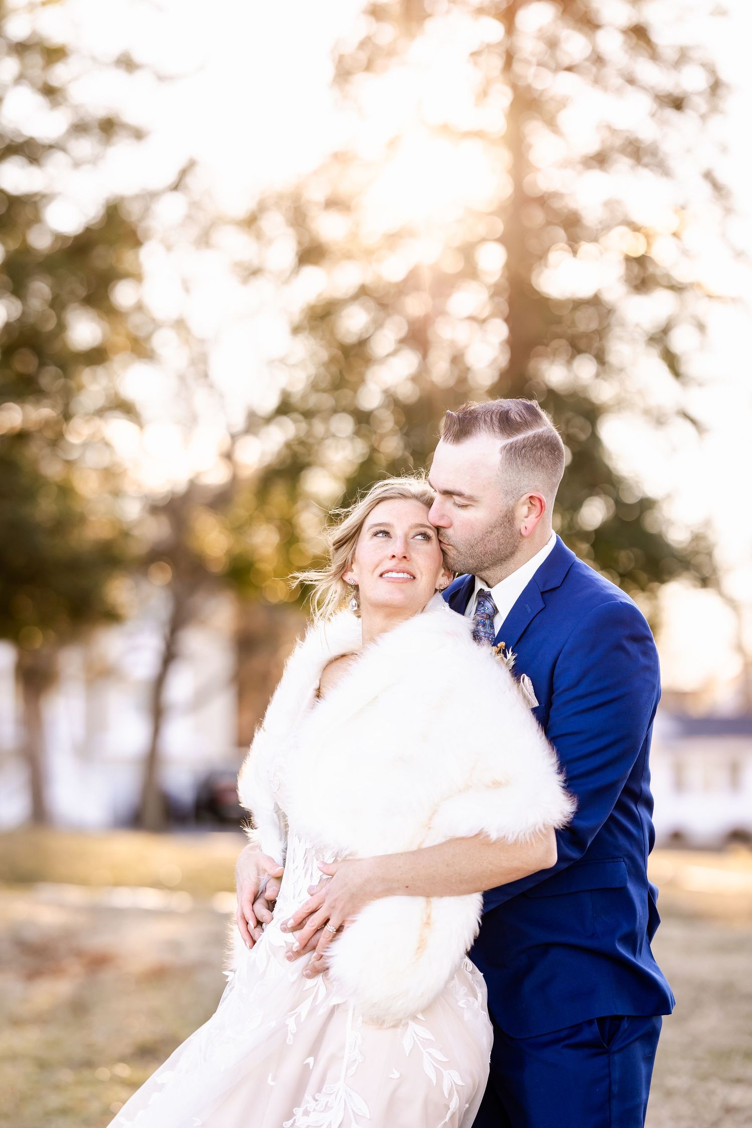 A joyful wedding couple share an intimate moment outdoors with golden sunlight filtering through trees behind them.