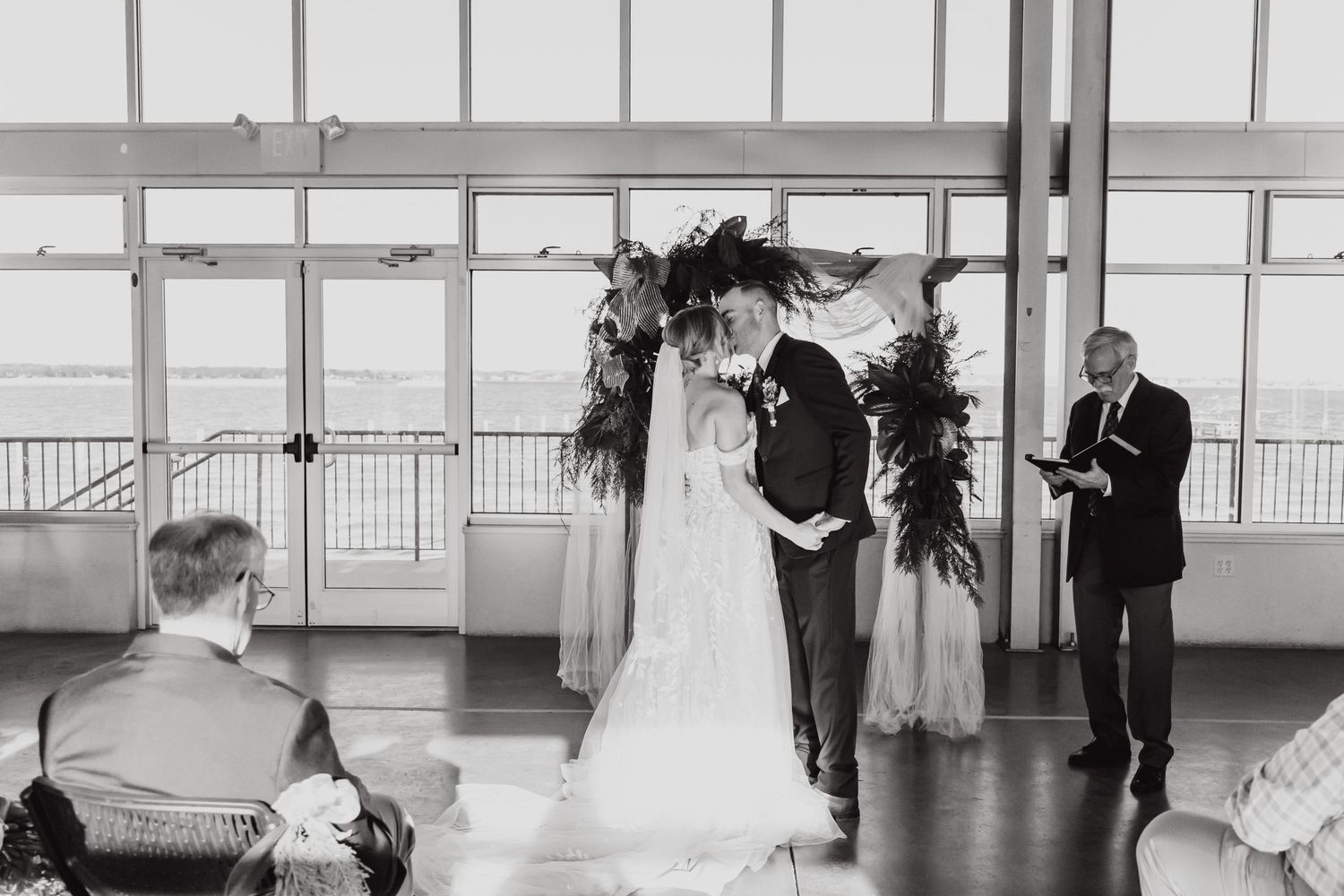 Black and white photo of a wedding ceremony in a modern venue with large windows.