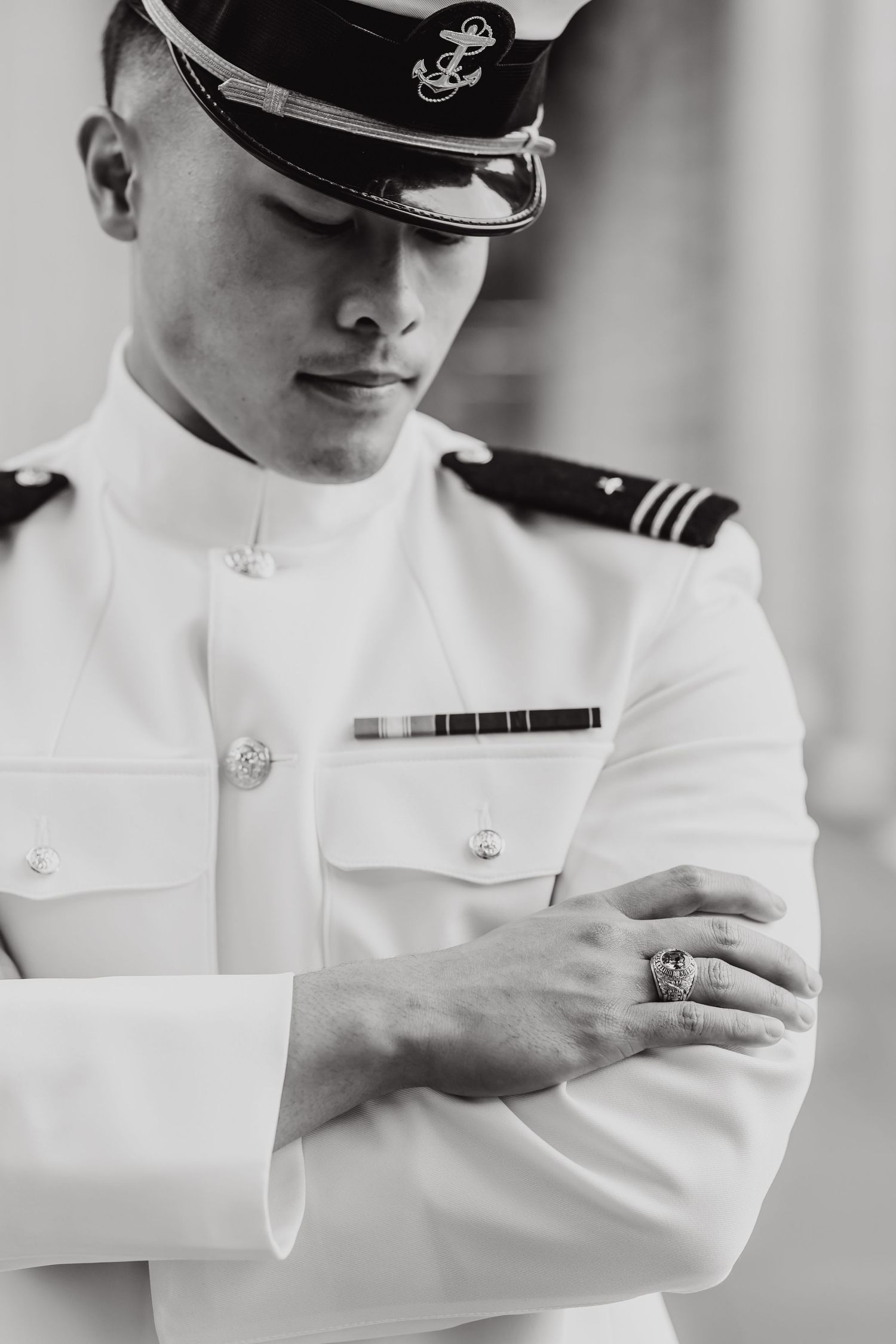 Naval officer in white dress uniform adjusting cuff detail in black and white portrait.