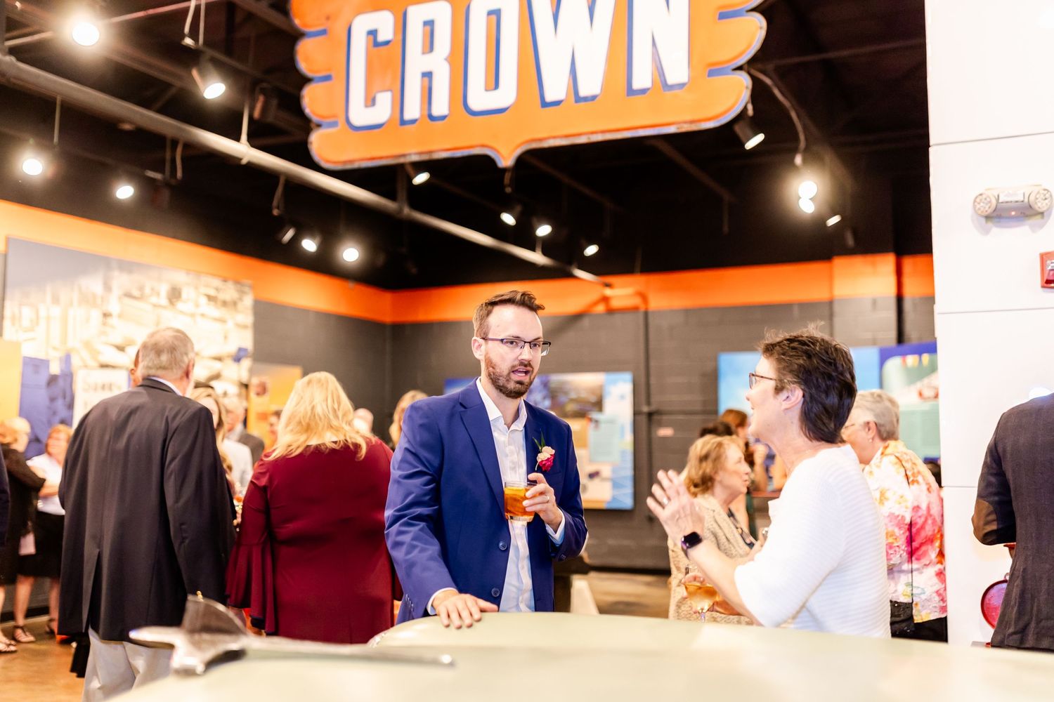Guests mingle at a reception space with orange signage reading 'Crown' overhead.