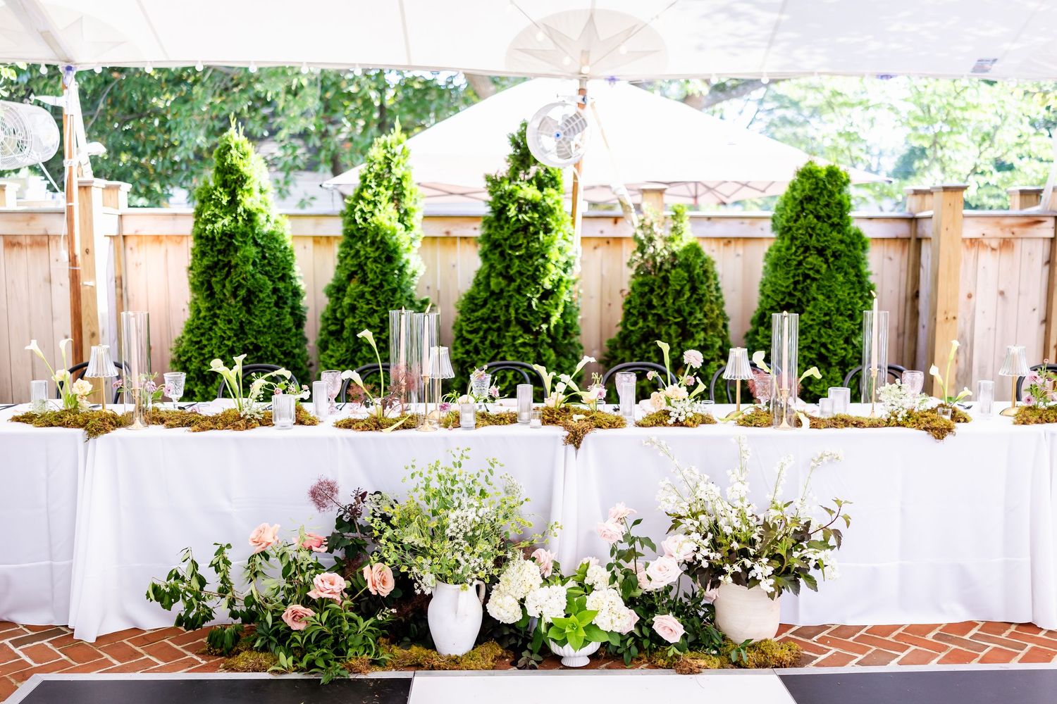 Garden terrace wedding reception setup with white tables and floral decorations.