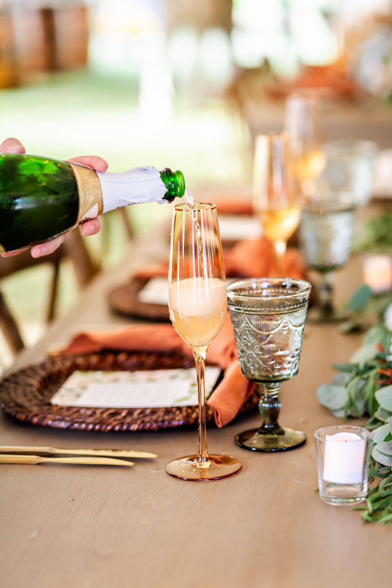 Elegant table settings with coral napkins, greenery, and vintage glassware at a wedding reception.