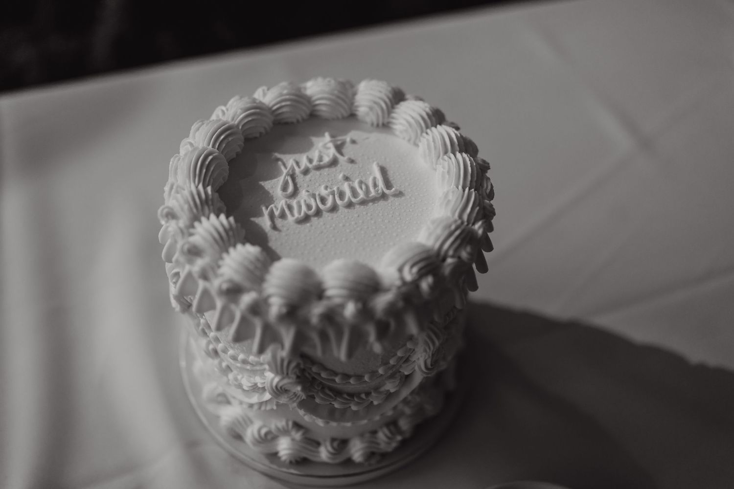 A classic white wedding cake with detailed piping photographed in black and white.