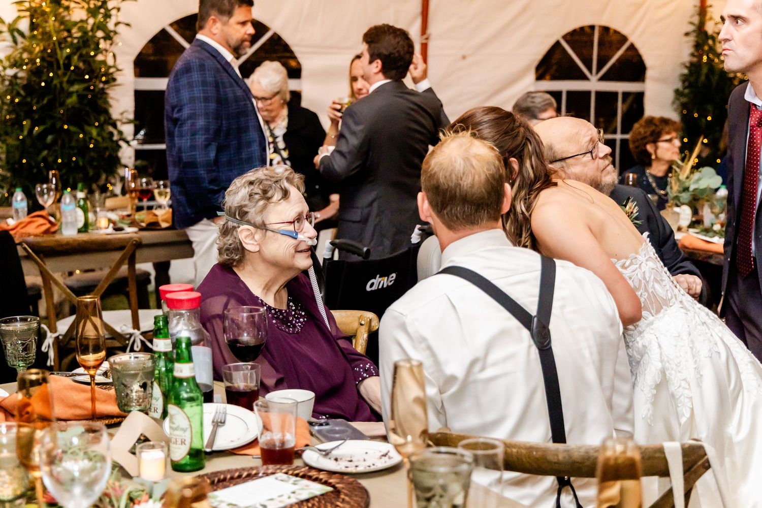 Wedding reception dinner guests seated at long tables with glowing lights and greenery decorations.