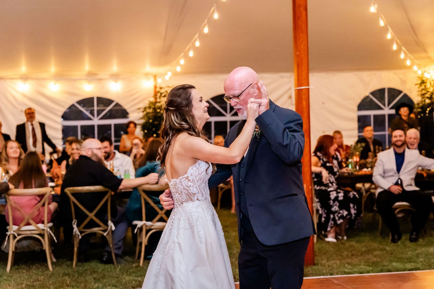 Festive wedding reception dance floor under a white tent with string lights creating a magical atmosphere.