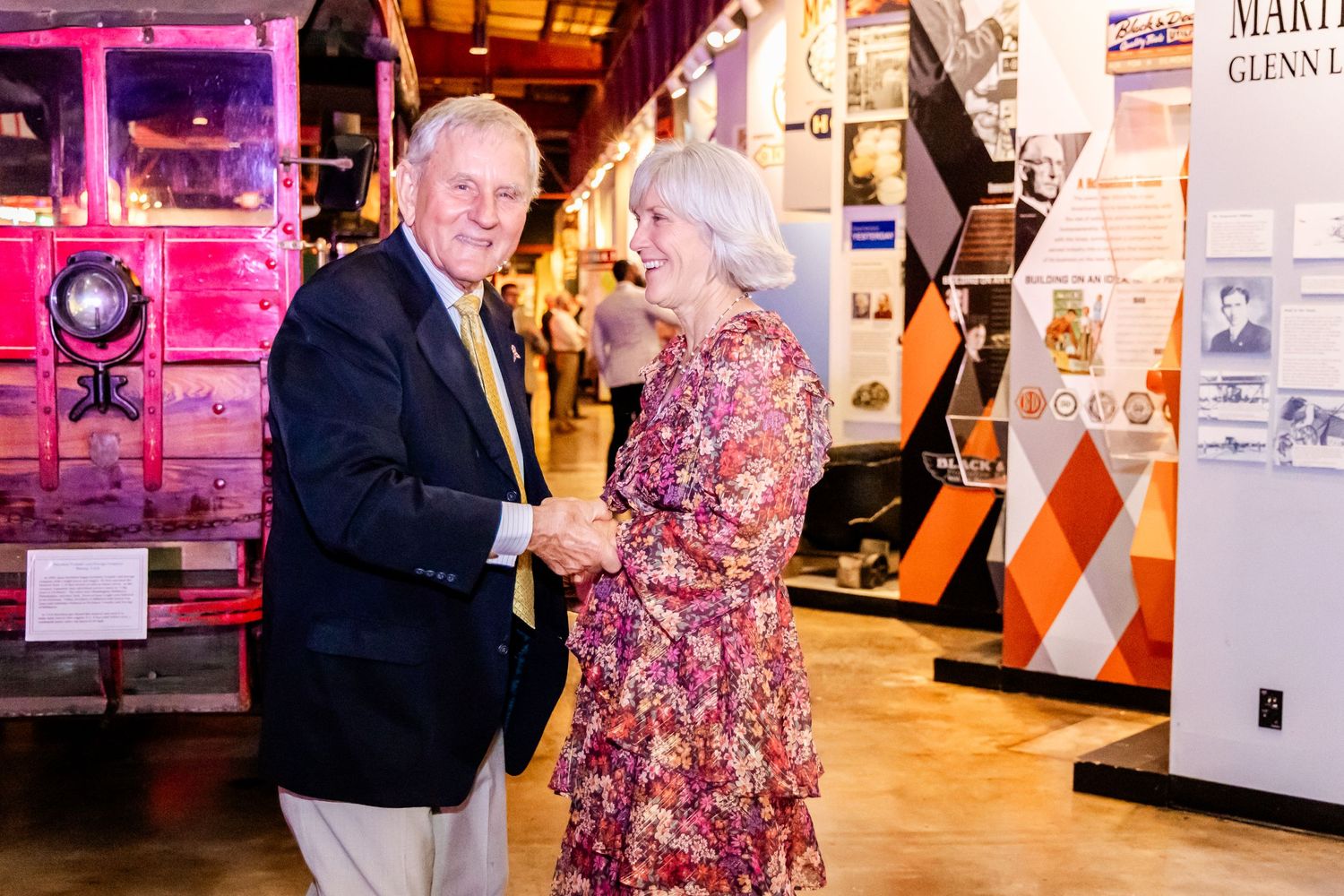 Two people dance together in formal attire with pink lighting and vintage decor in the background.