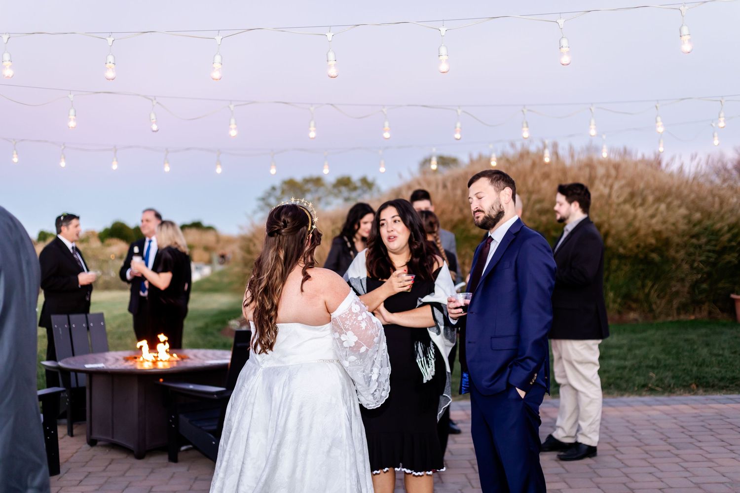 Wedding reception guests gather on outdoor patio with string lights at dusk.