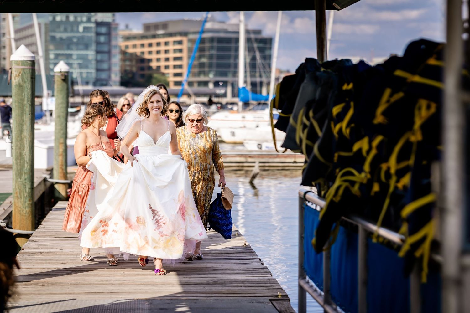 Wedding party walking along a marina dock with boats in the background.