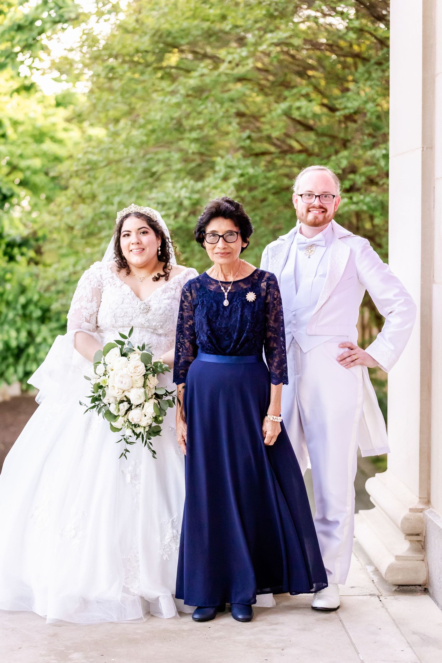 A wedding party poses outdoors with the bride in white and wedding party member in navy blue formal attire.
