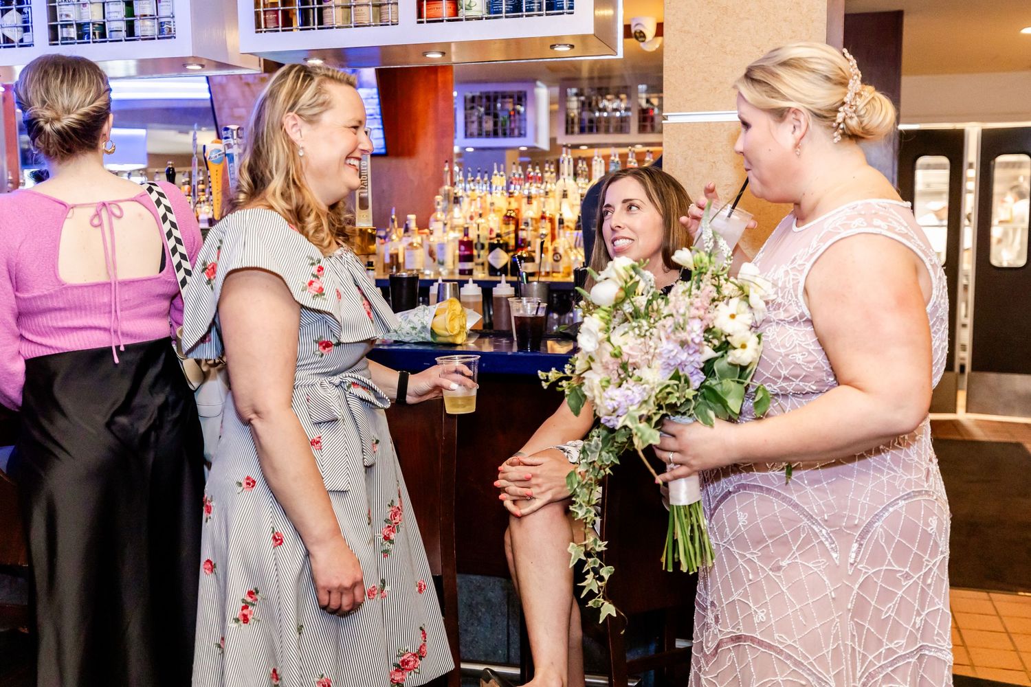 Group of guests chatting and celebrating at a bar with floral arrangements.