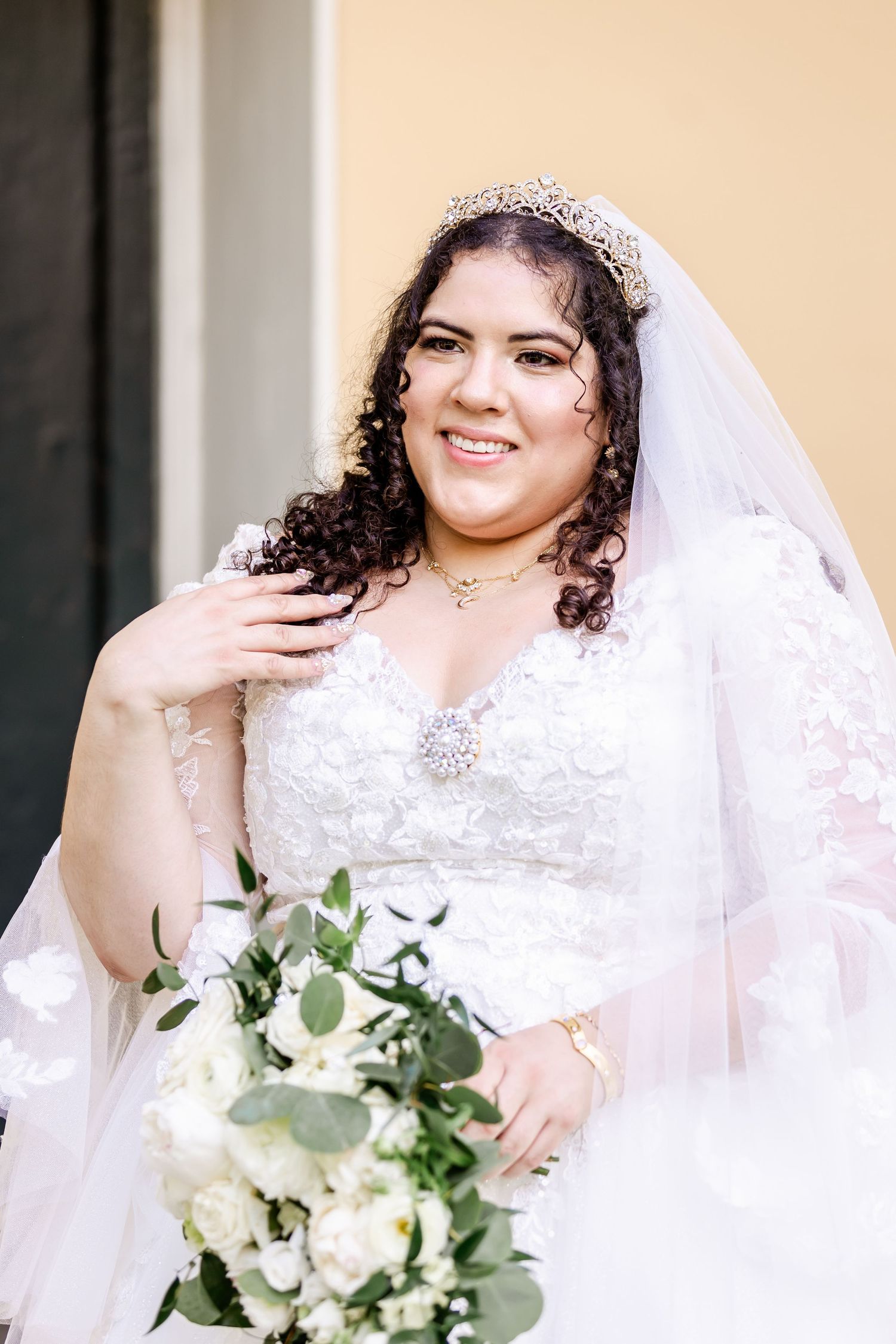 Wedding portrait showing a detailed lace gown, crystal tiara, and cascading bouquet of white flowers and greenery.