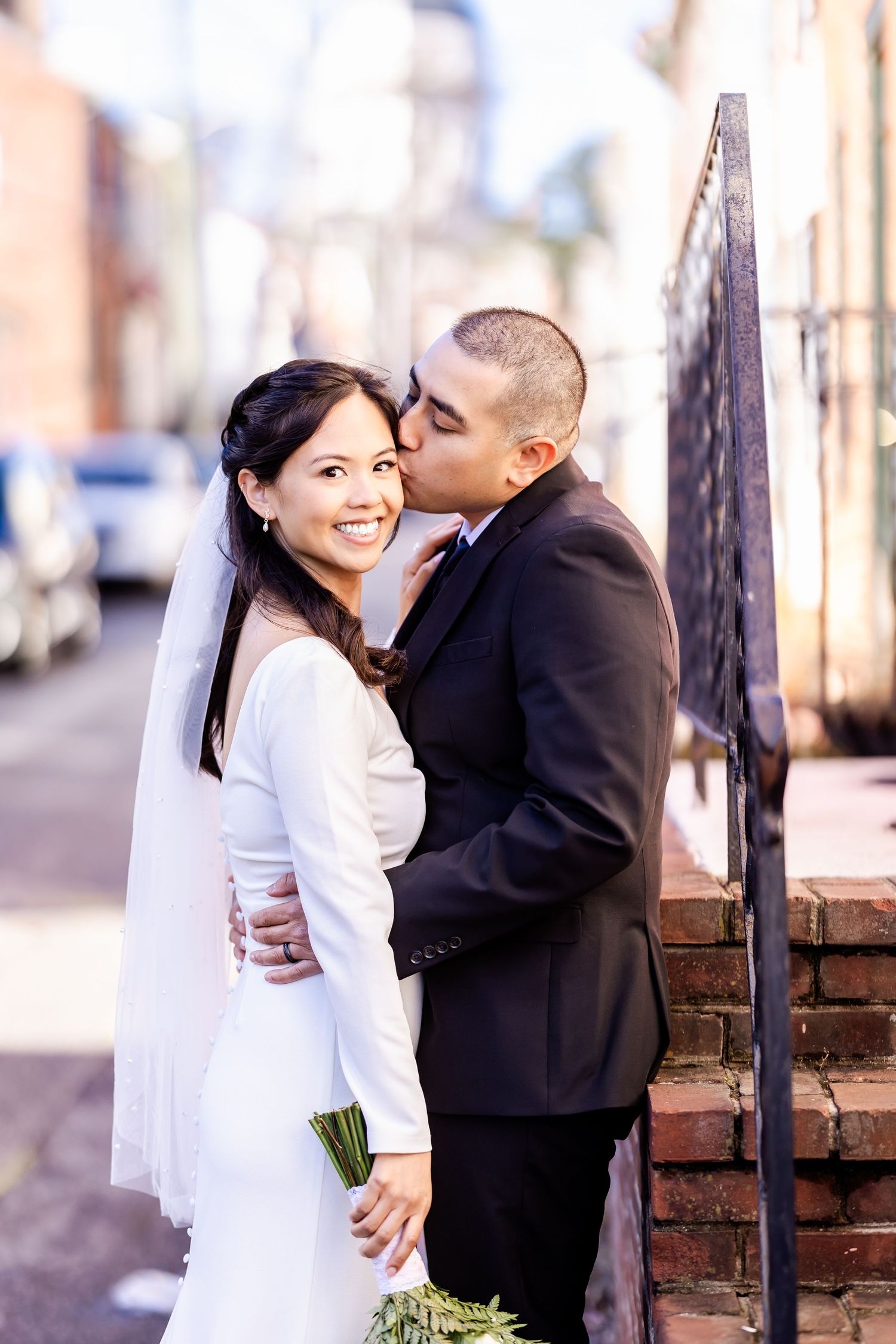 A romantic wedding photo captured in an urban setting with brick buildings and archways.