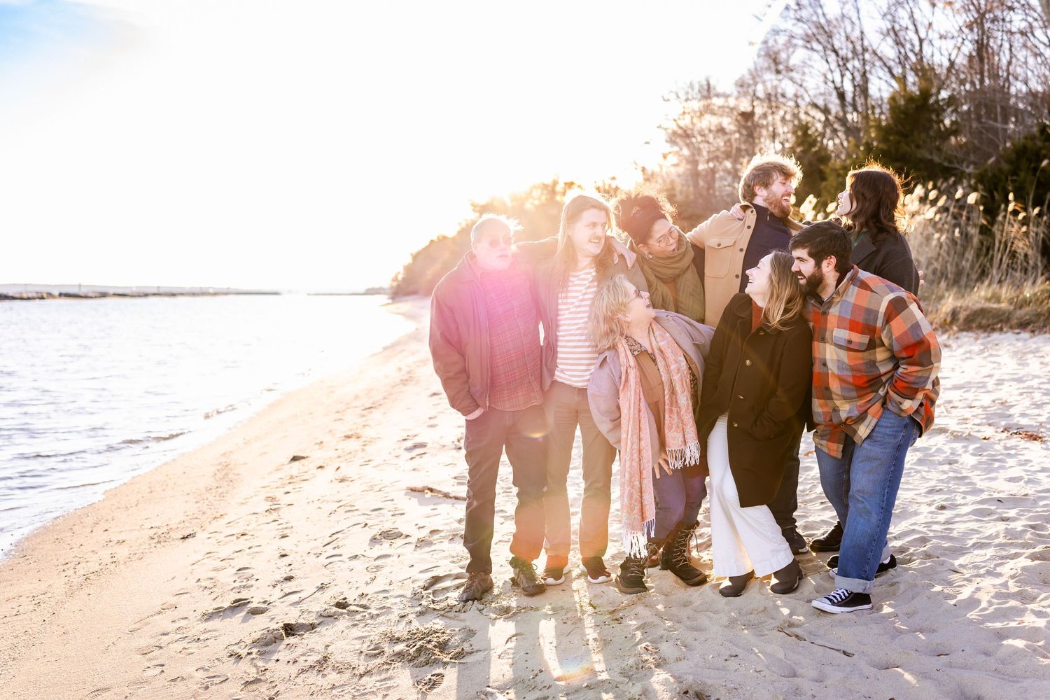 Group poses together on beach at sunset with water and trees in background.
