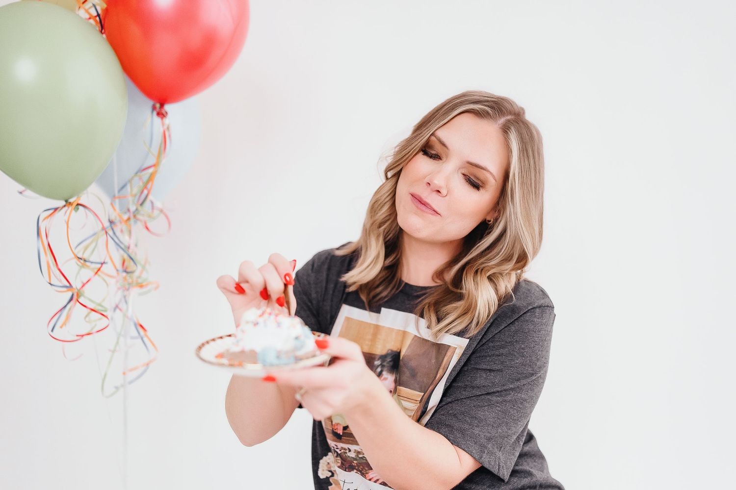 A person in a gray sweater poses playfully with colorful balloons against a white background.