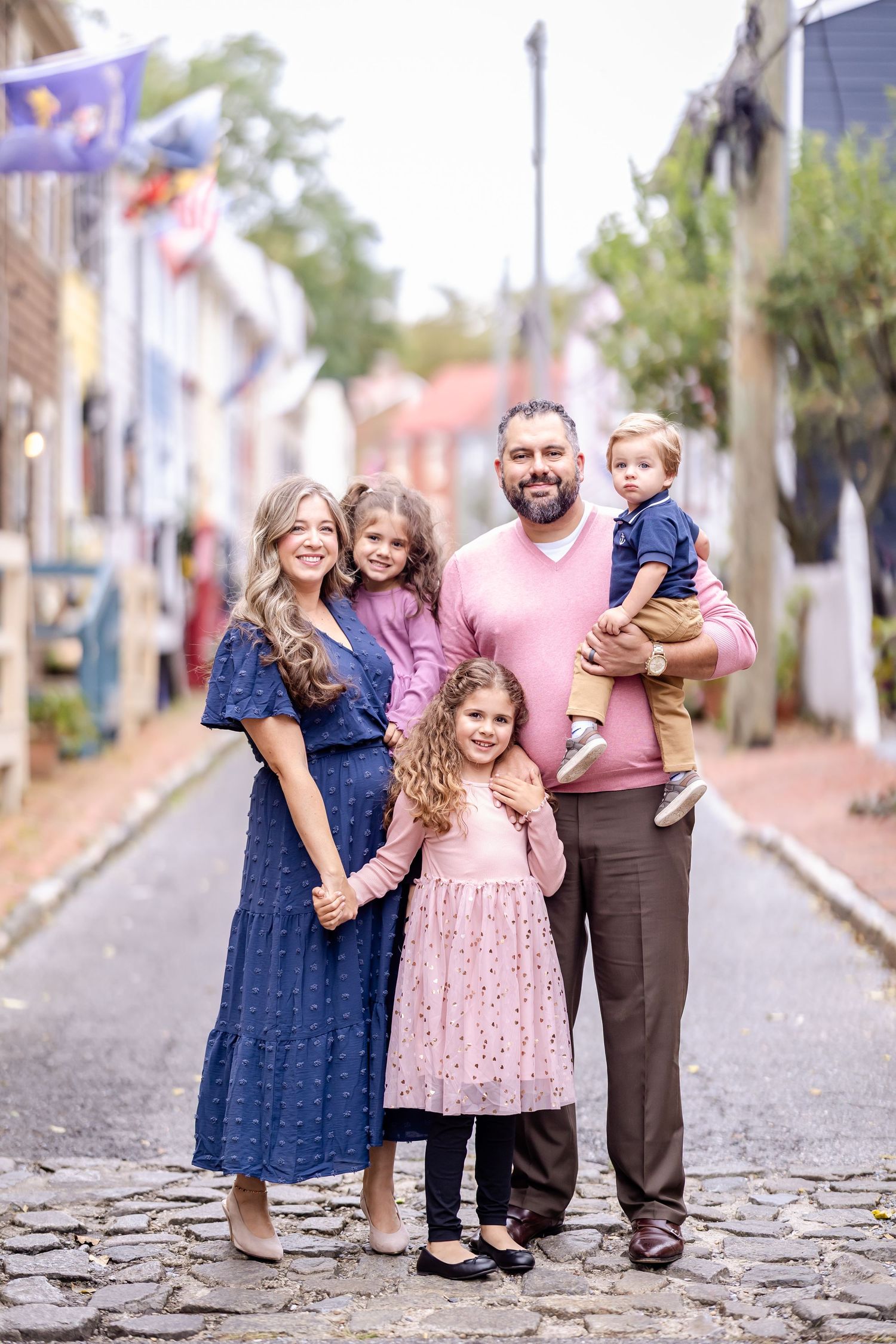 A group stands together on a cobblestone street while wearing blue and pink dresses and brown pants.