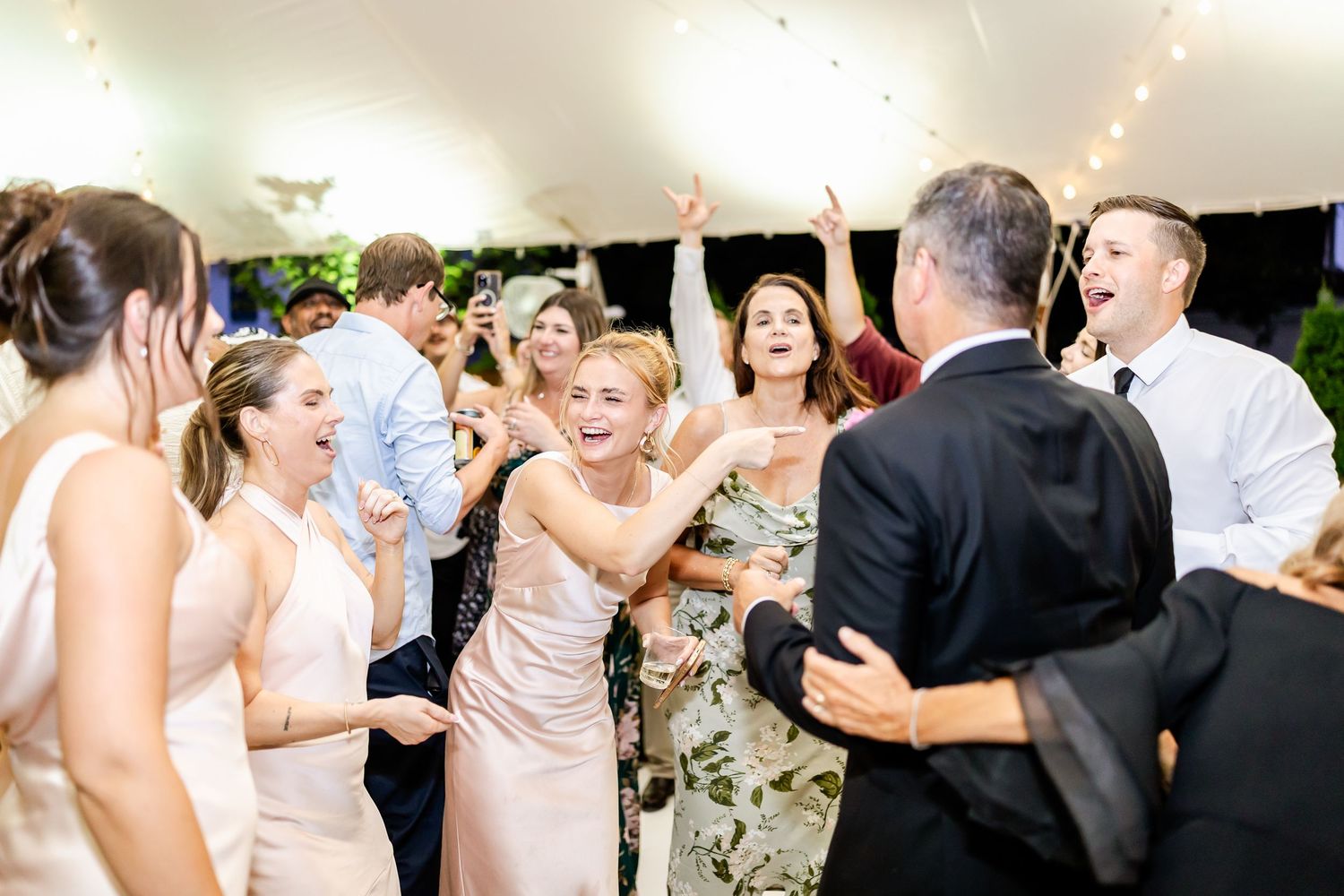 Joyful wedding reception guests dancing and celebrating under indoor lighting.