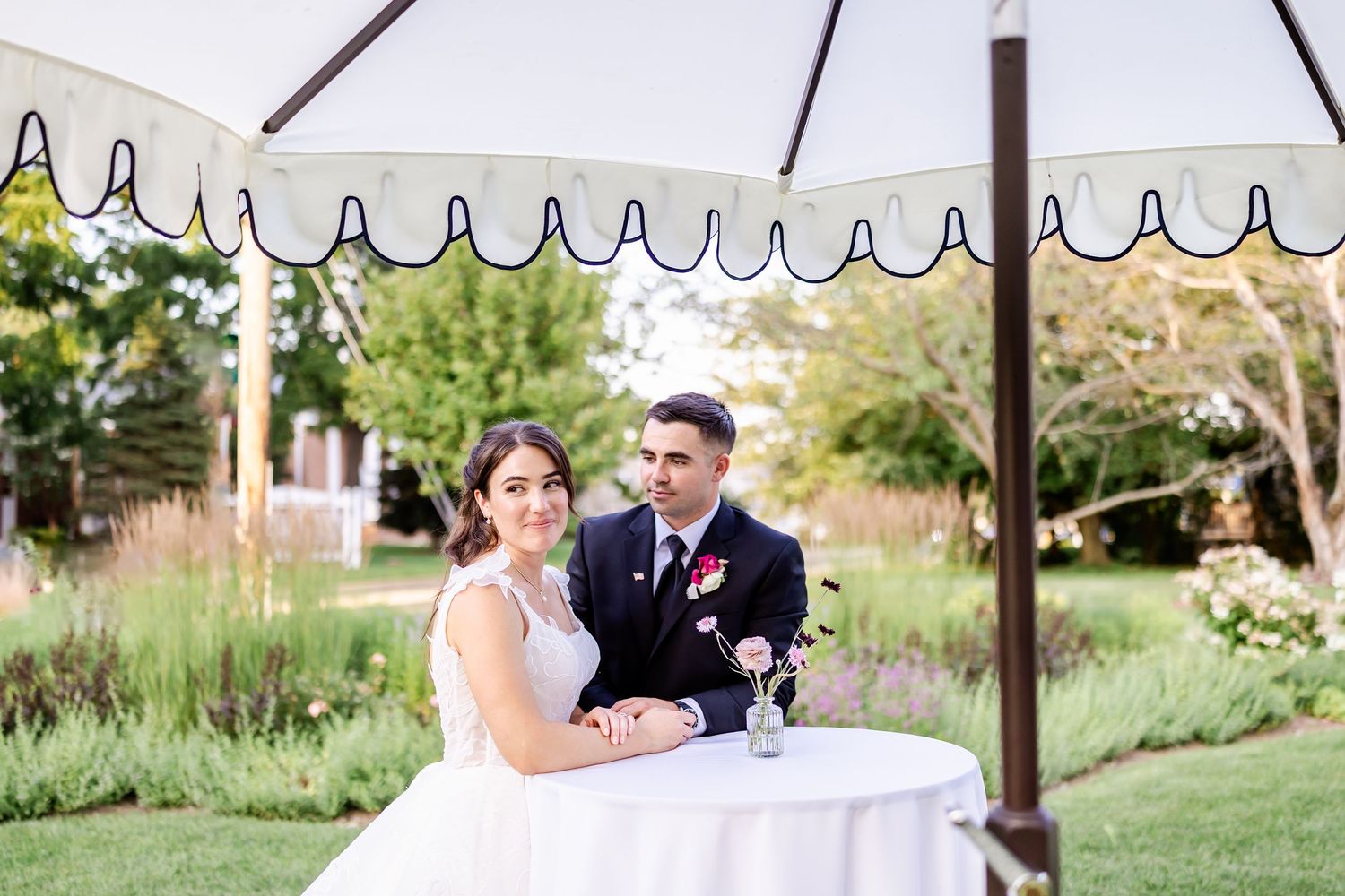 Elegant outdoor wedding seating arrangement with white umbrellas and garden backdrop.