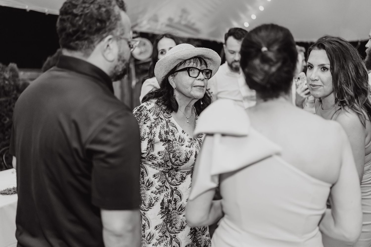 A black and white photo shows a group of people engaged in conversation at what appears to be a social gathering.