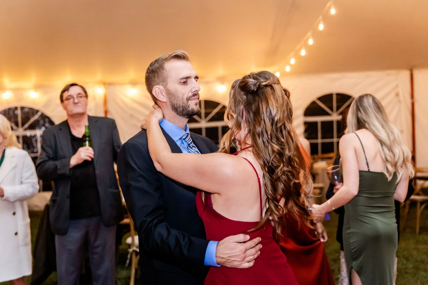 Wedding guests dancing and socializing at an evening reception with warm lighting and string lights.