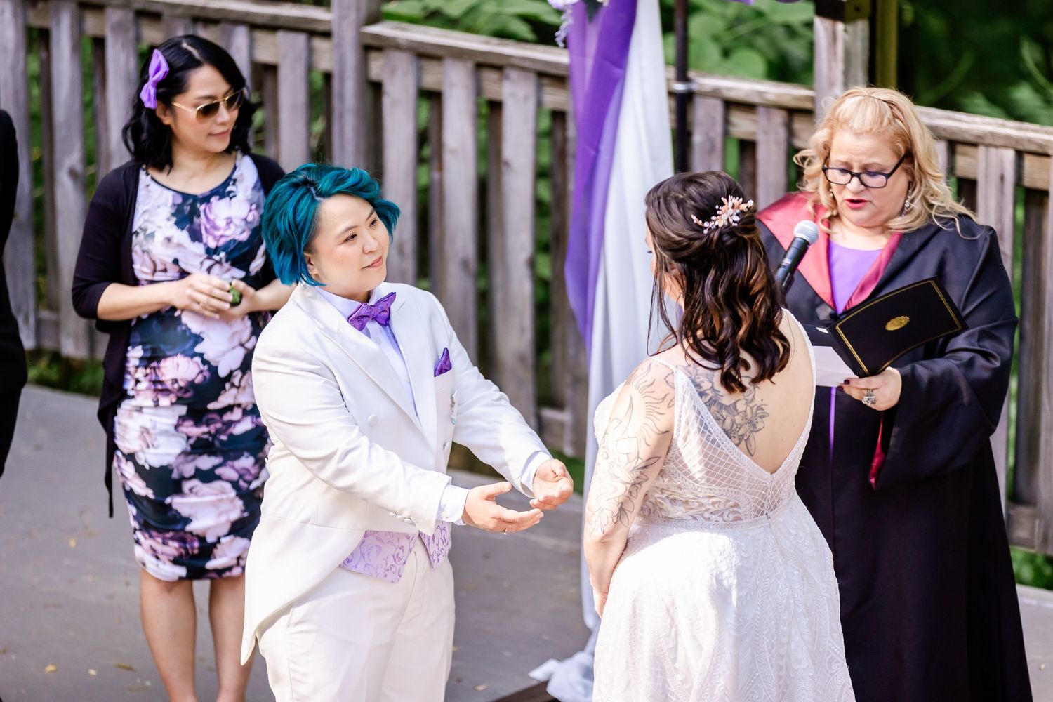 A candid ceremony moment between wedding participants under a purple-decorated arch.
