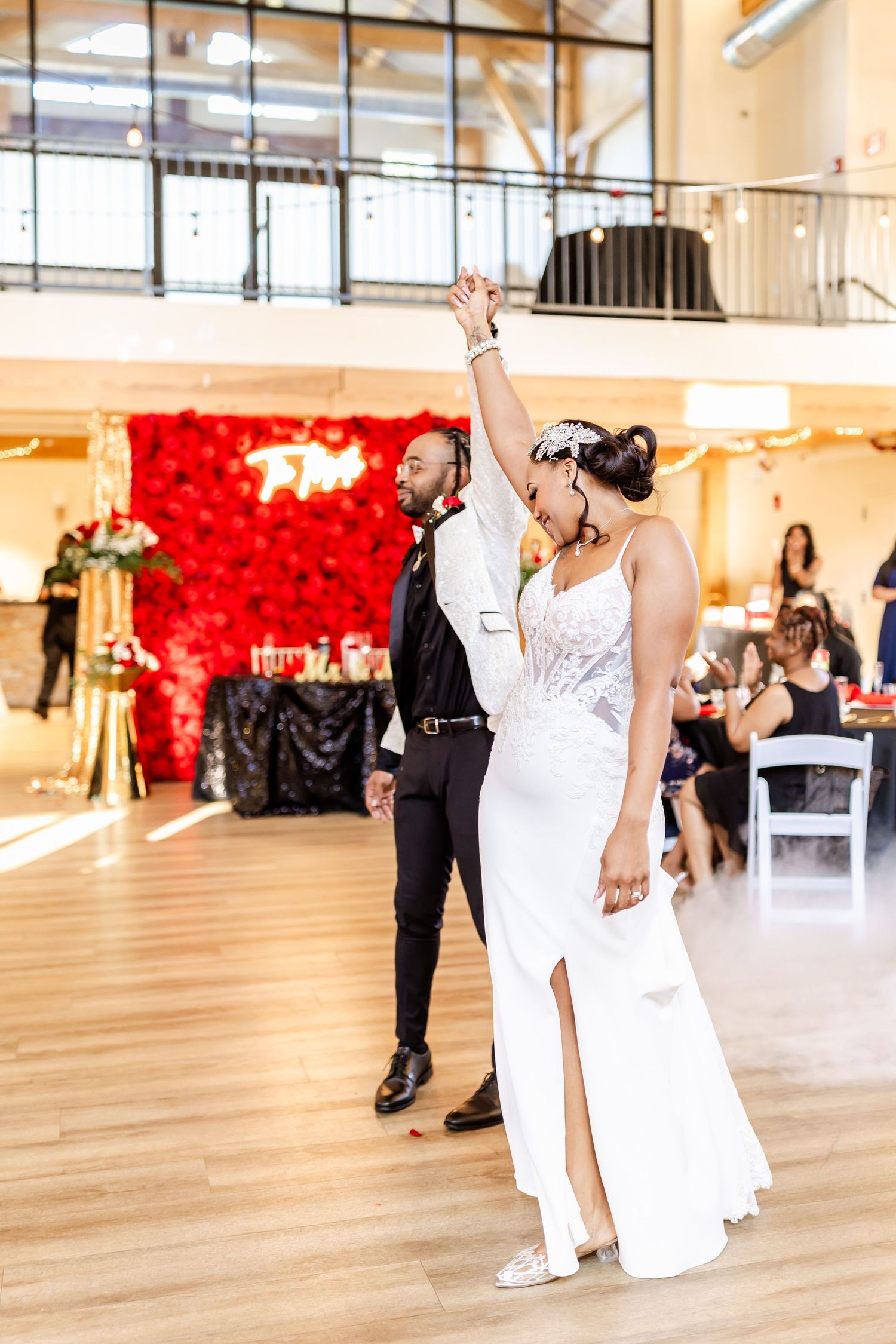 Elegant wedding dance with couple in white and black attire against red floral wall.