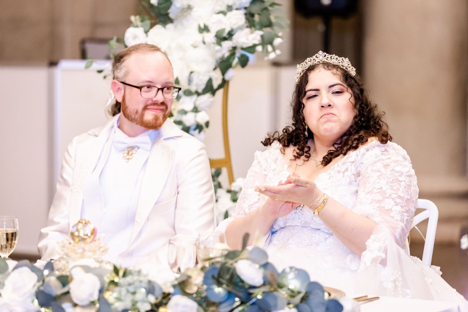 Couple enjoys meal at decorated head table during wedding reception.