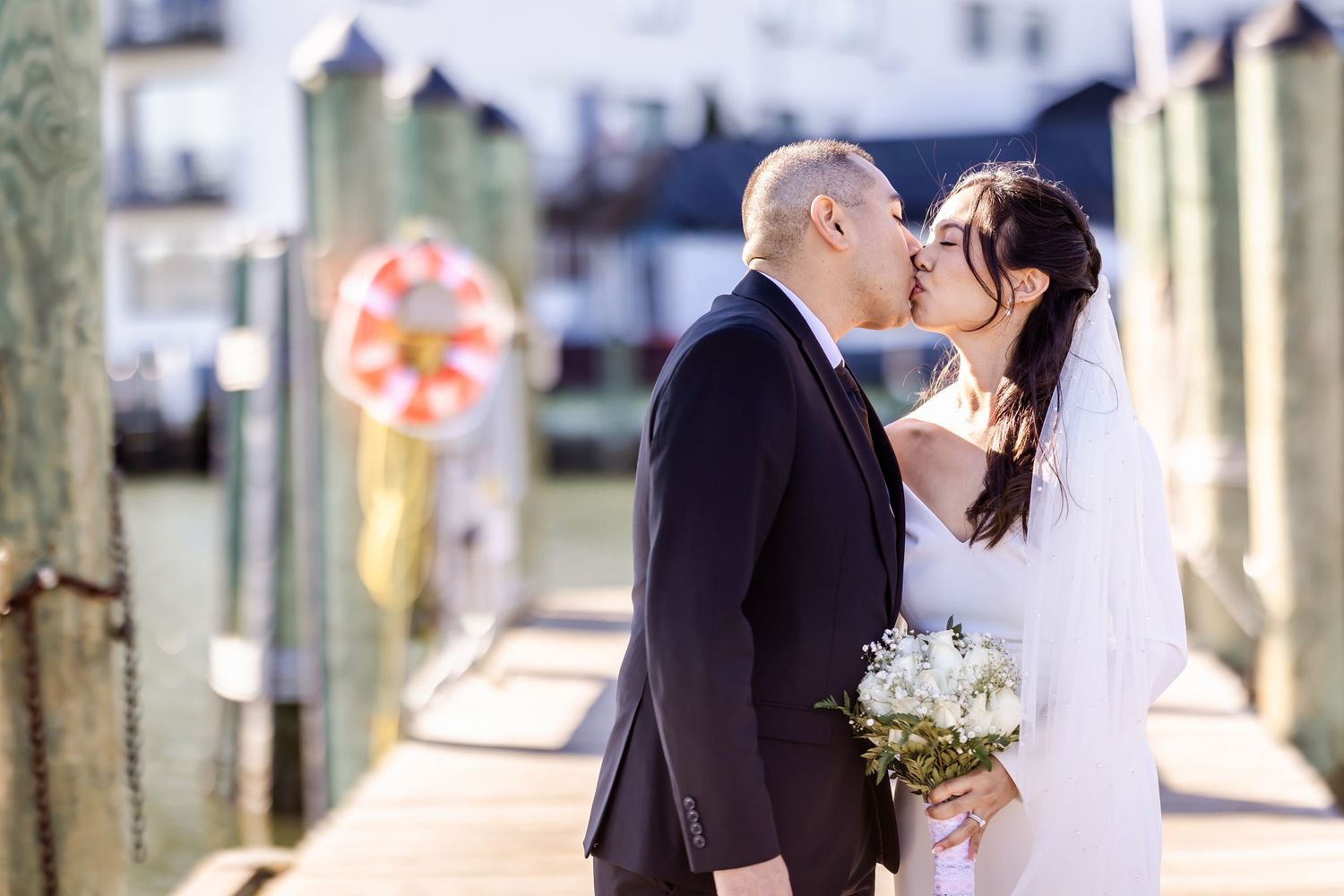 Romantic wedding moment captured on a scenic dock with a life preserver and waterfront buildings.