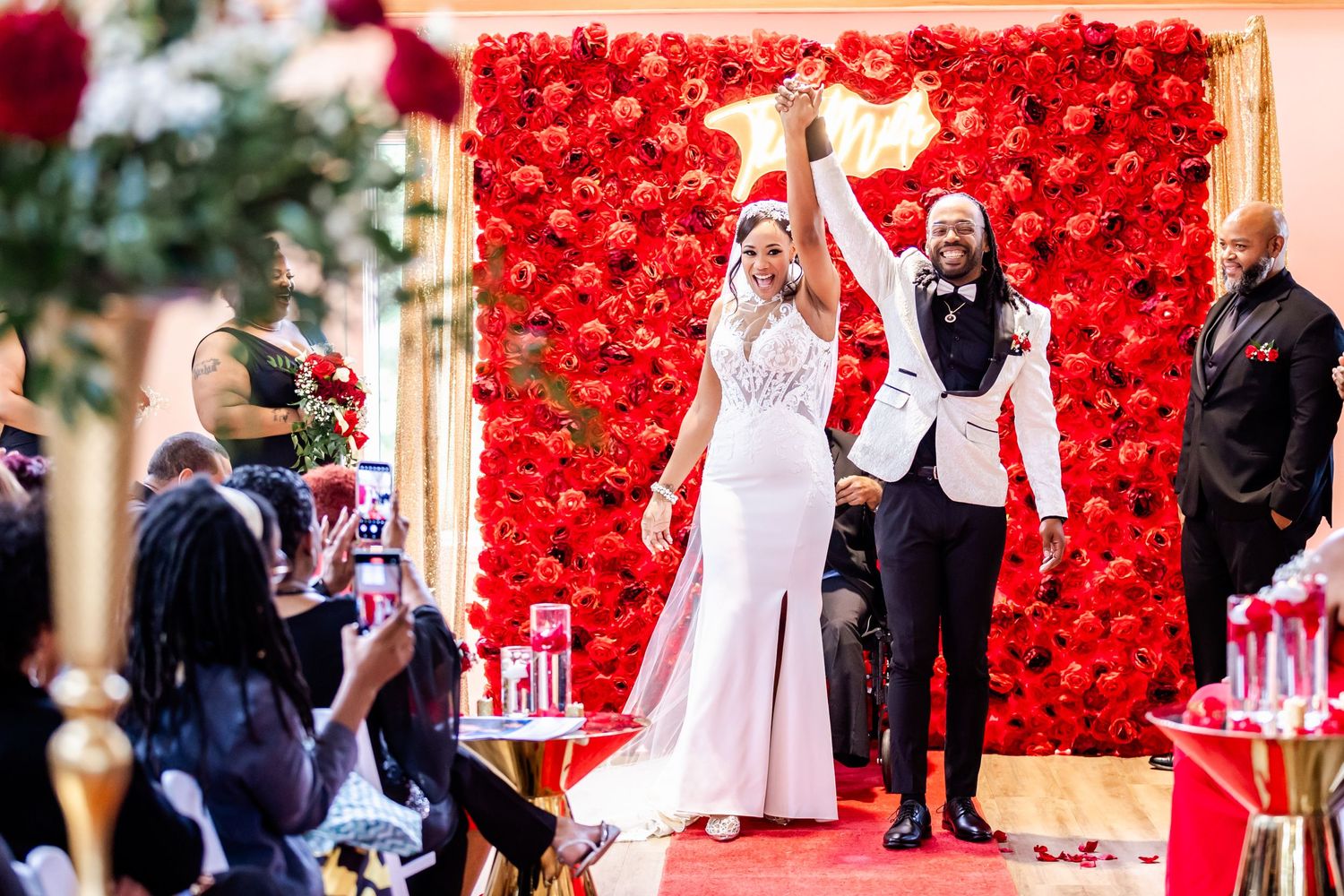 Celebratory moment during wedding ceremony against vibrant red rose backdrop.