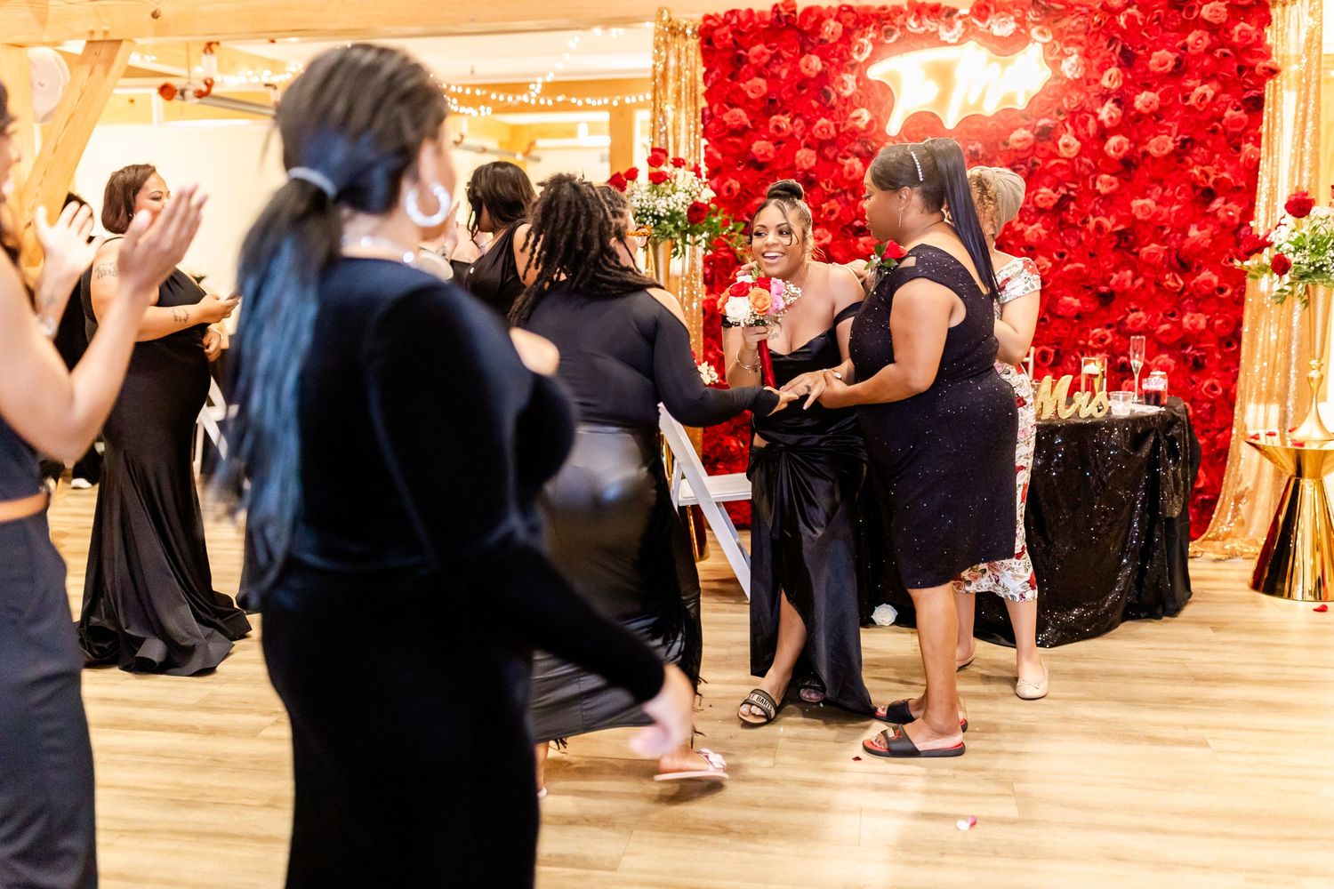 Wedding guests dancing at reception with dramatic red balloon wall decoration in background.