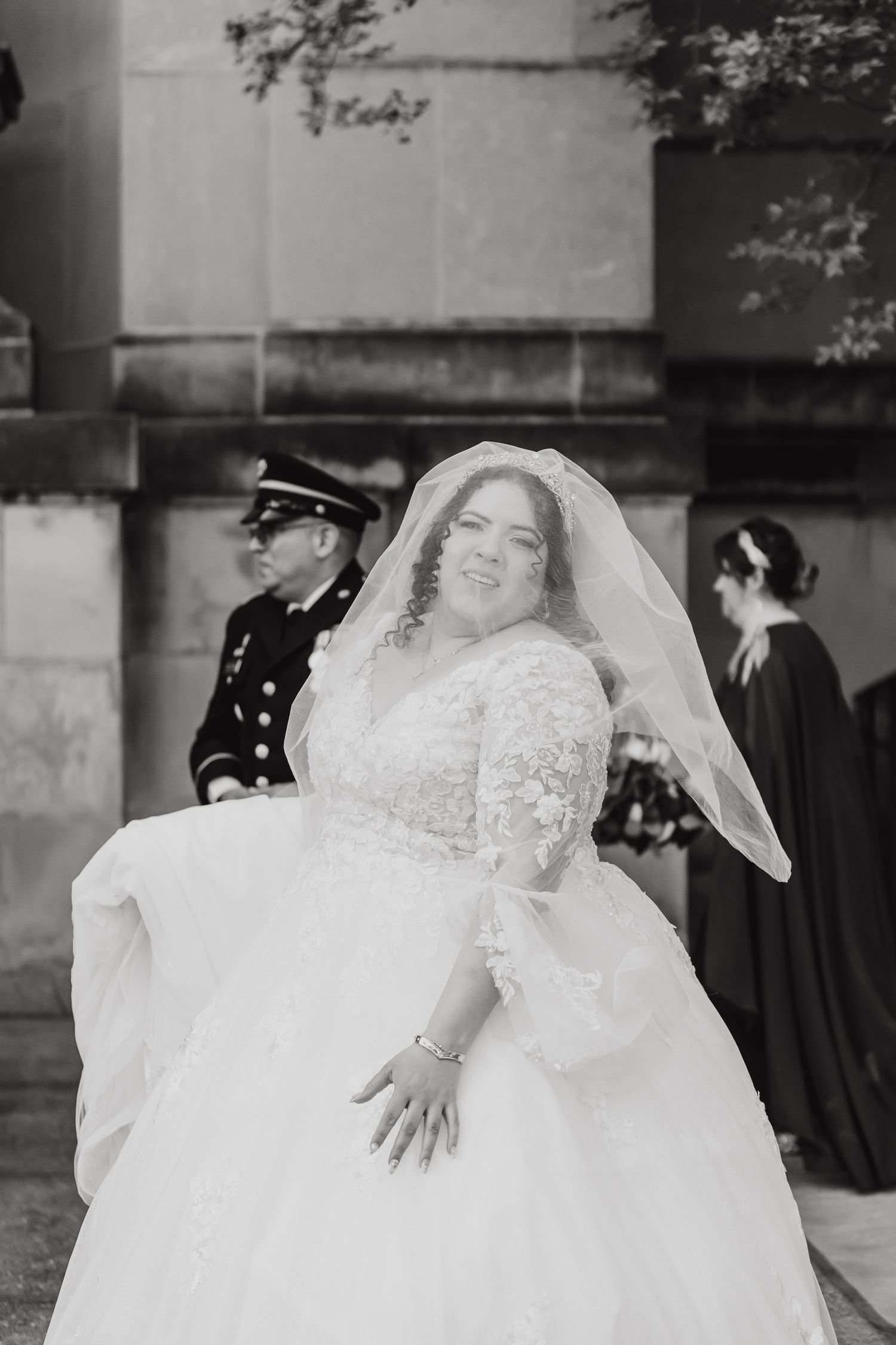 Black and white portrait of bride in lace wedding dress with flowing veil.