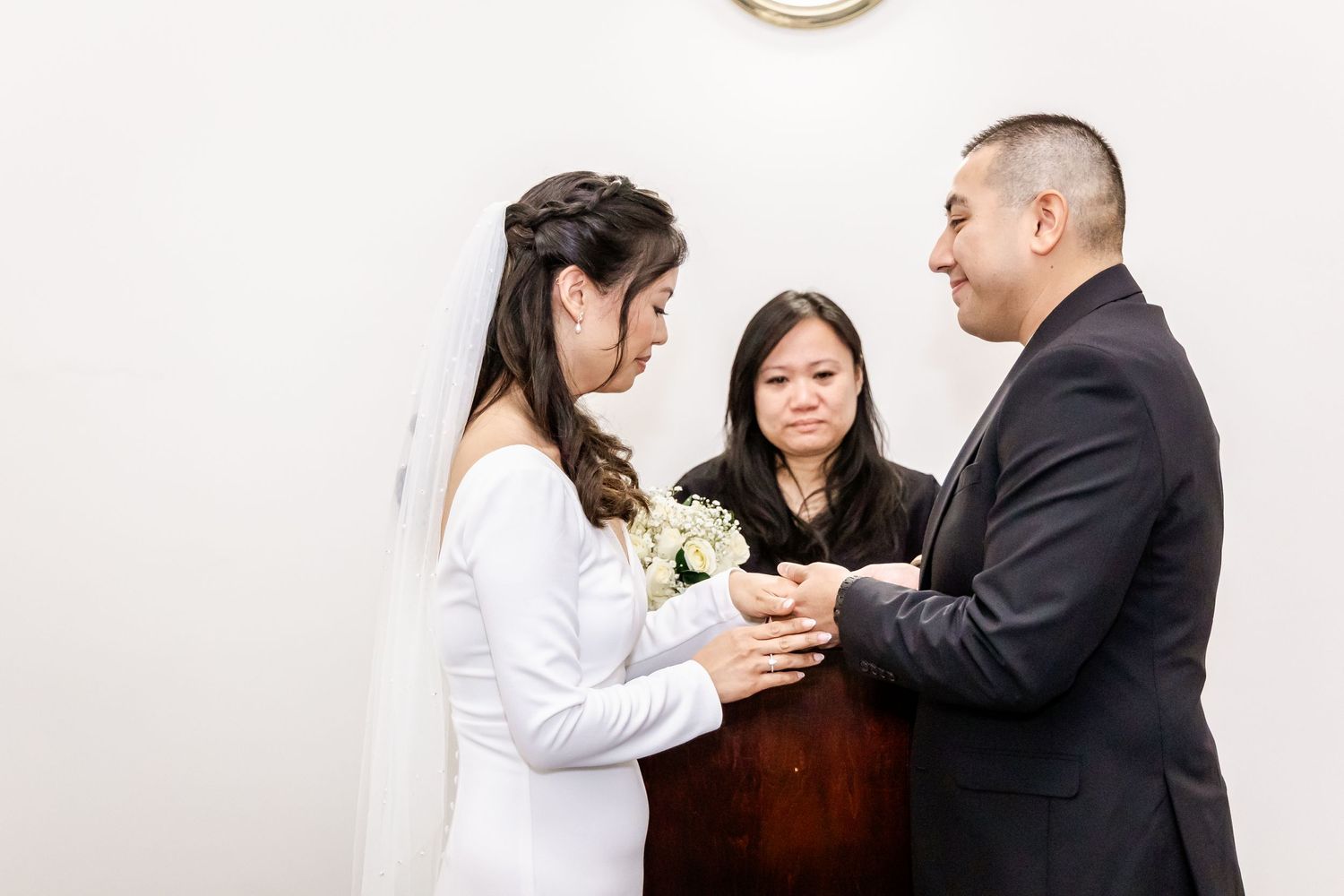 Wedding couple exchanges rings during their ceremony while the officiant guides the moment.