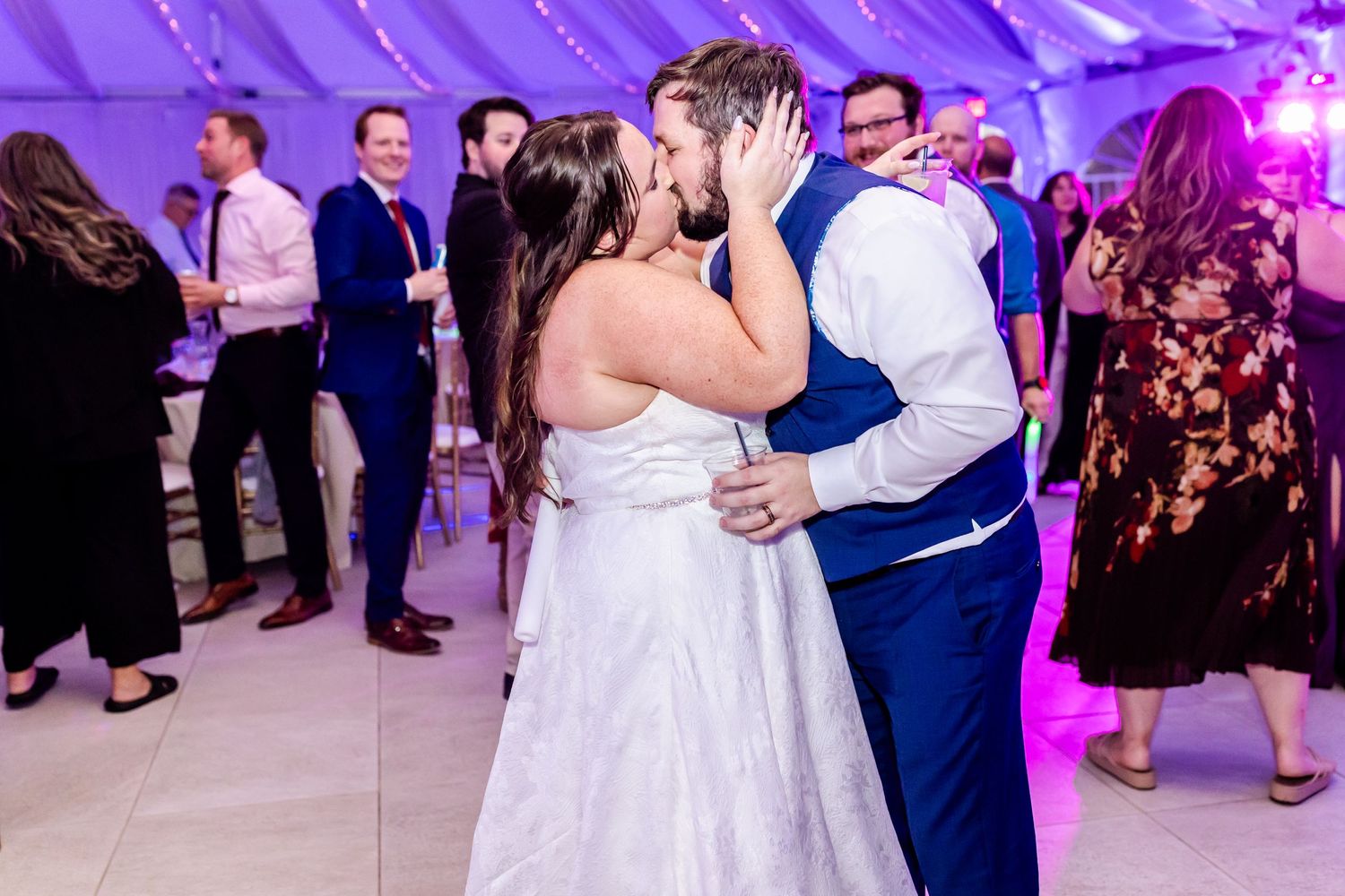 Couple embracing during romantic dance under purple lighting at wedding reception.