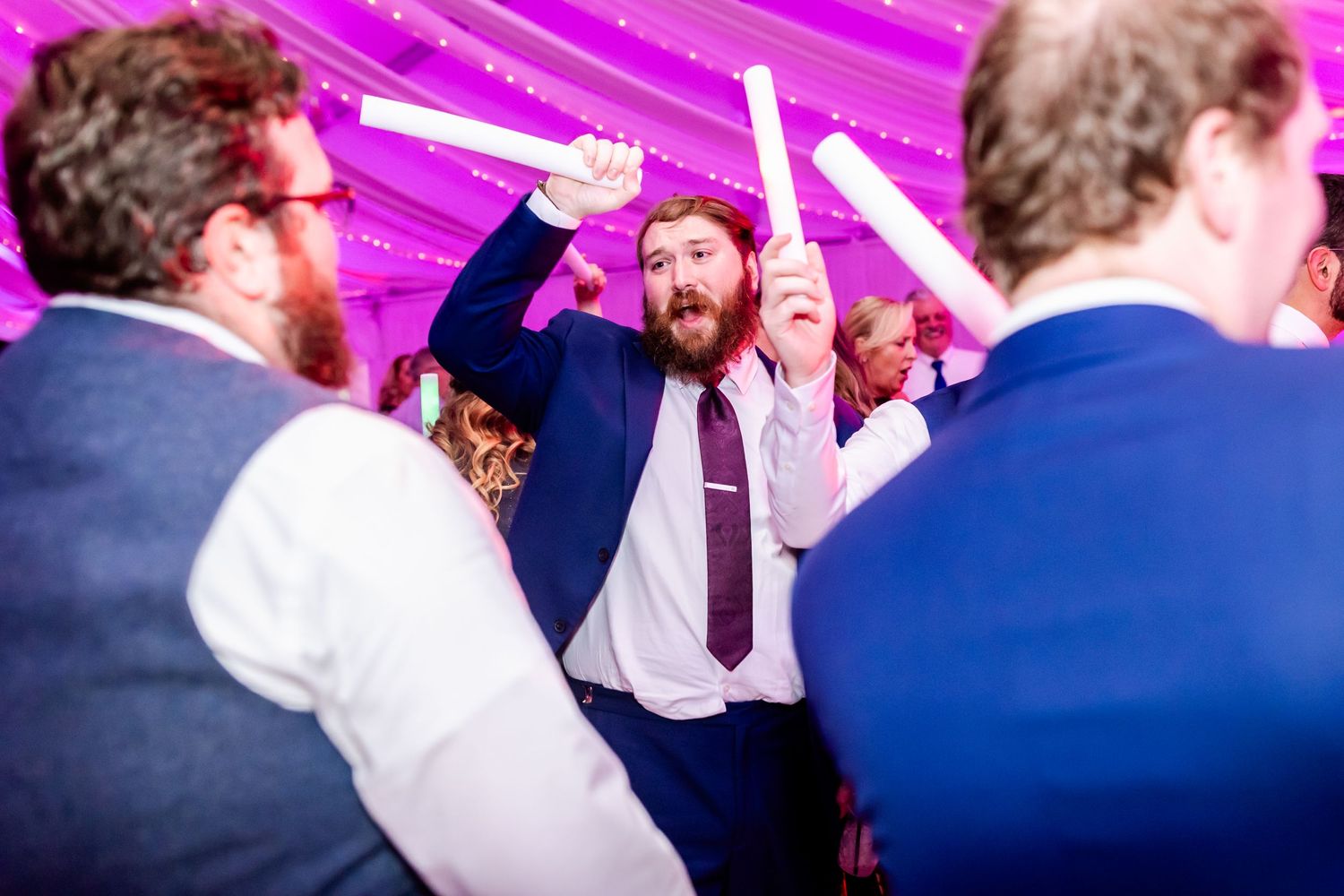 Energetic dance party scene with purple lighting and ceiling draping at wedding reception.