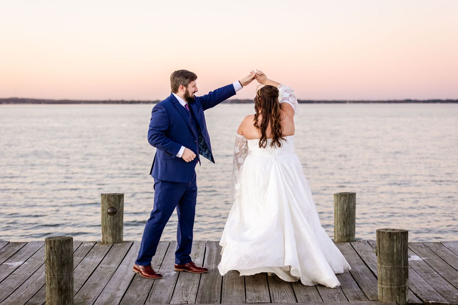 Newlyweds share a romantic dance together on a waterfront dock at dusk.