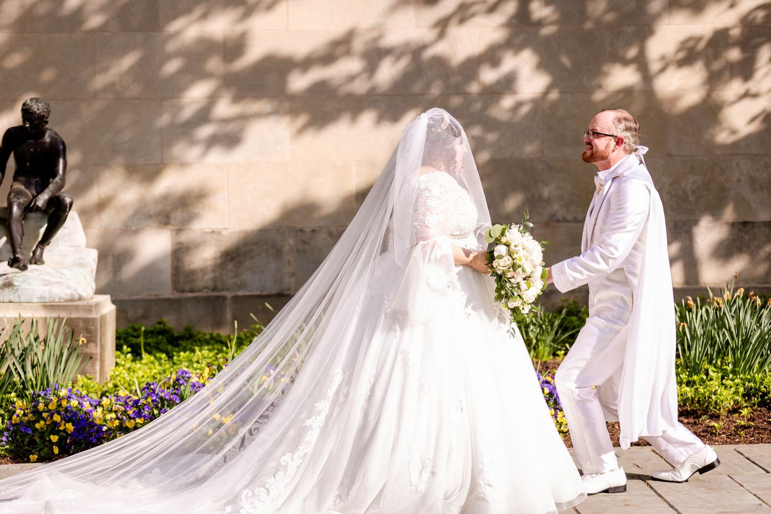 Long cathedral veil trails behind bride during intimate garden wedding ceremony.