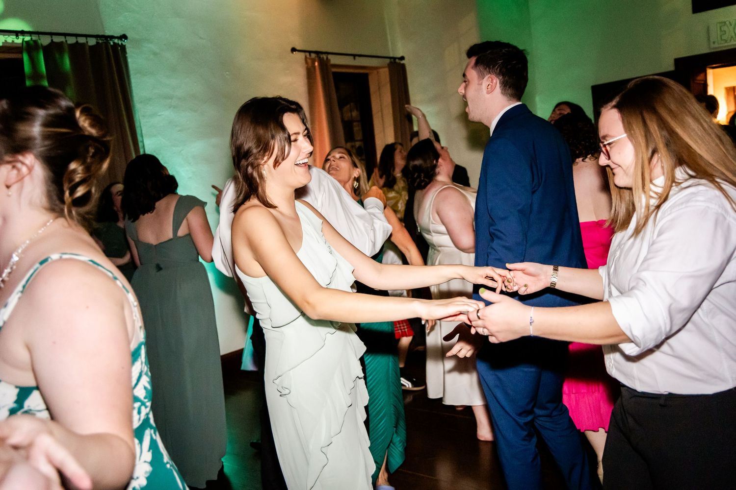 Wedding reception dance party with guests celebrating on the dance floor under green and orange lighting.