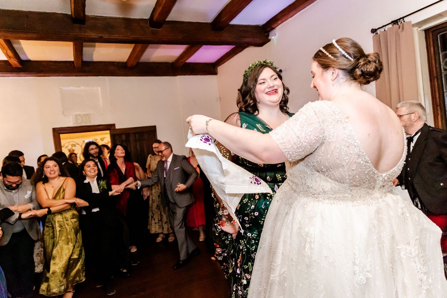 Wedding reception dance floor filled with guests watching two people dancing in a rustic indoor venue.