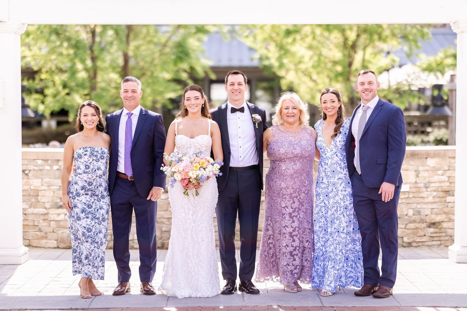 Wedding party in blue floral dresses and formal attire posed together outdoors.