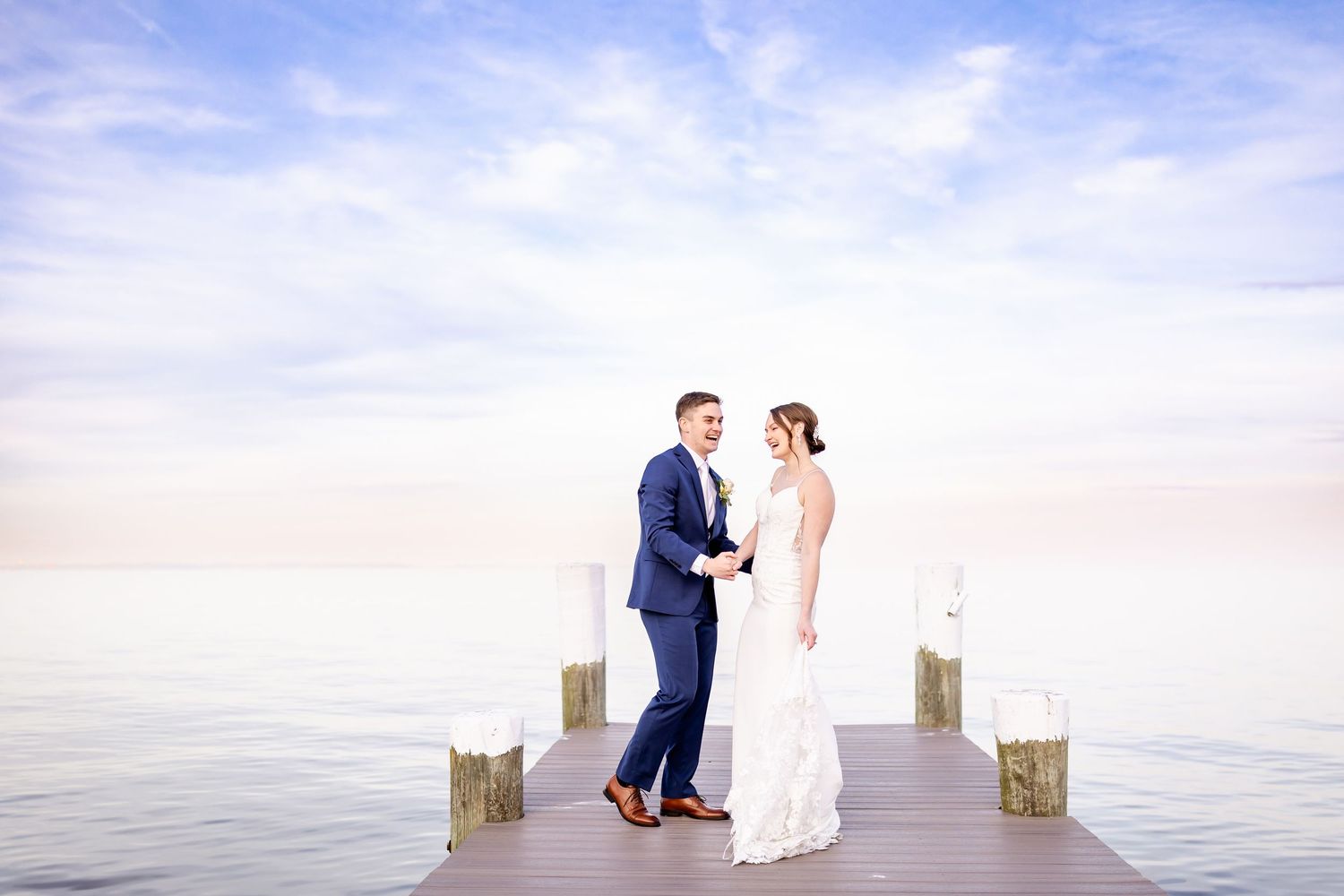 Wedding couple stands together on wooden dock over calm waters during golden hour.