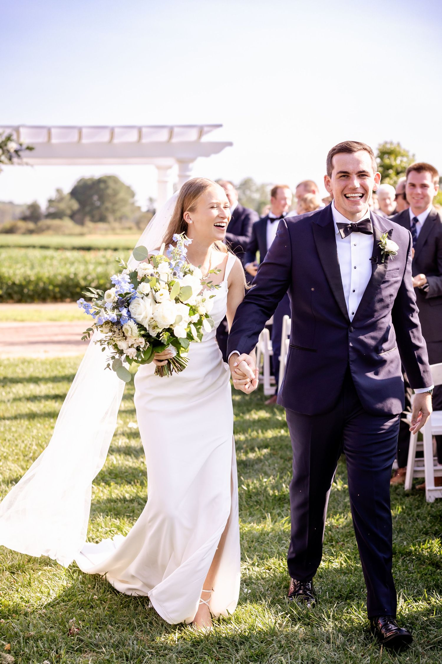 A joyful wedding party walks and laughs together on a grassy lawn during an outdoor ceremony.