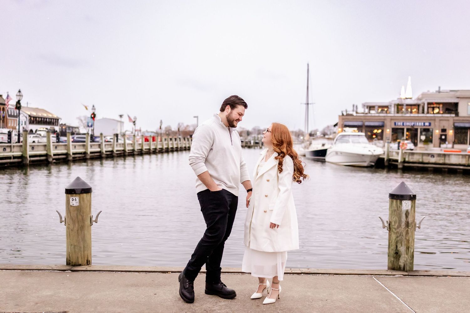 A couple shares a romantic moment together on a wooden dock overlooking a marina at sunset.
