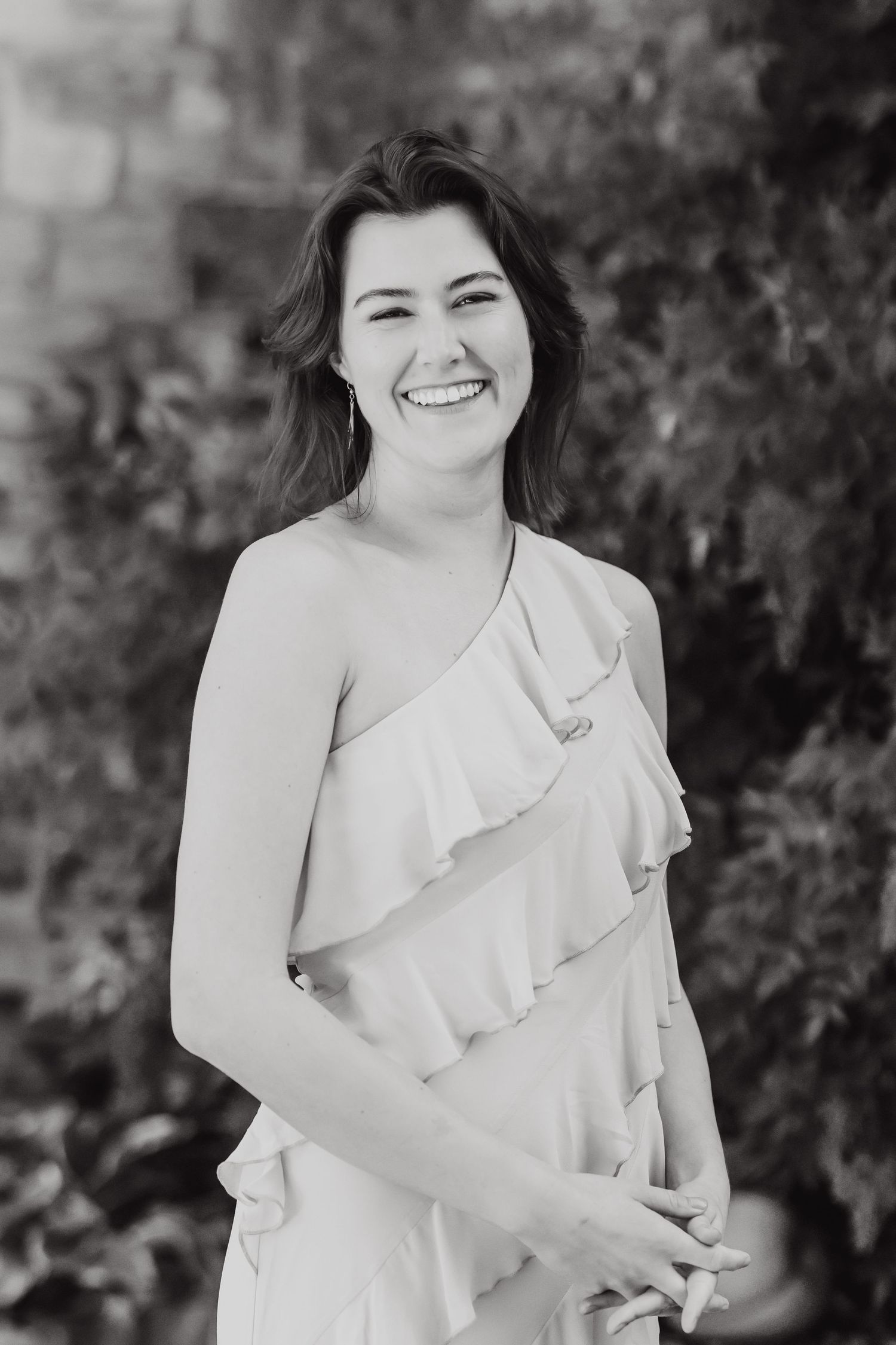 Black and white portrait photo of a woman in a light ruffled dress smiling outdoors.